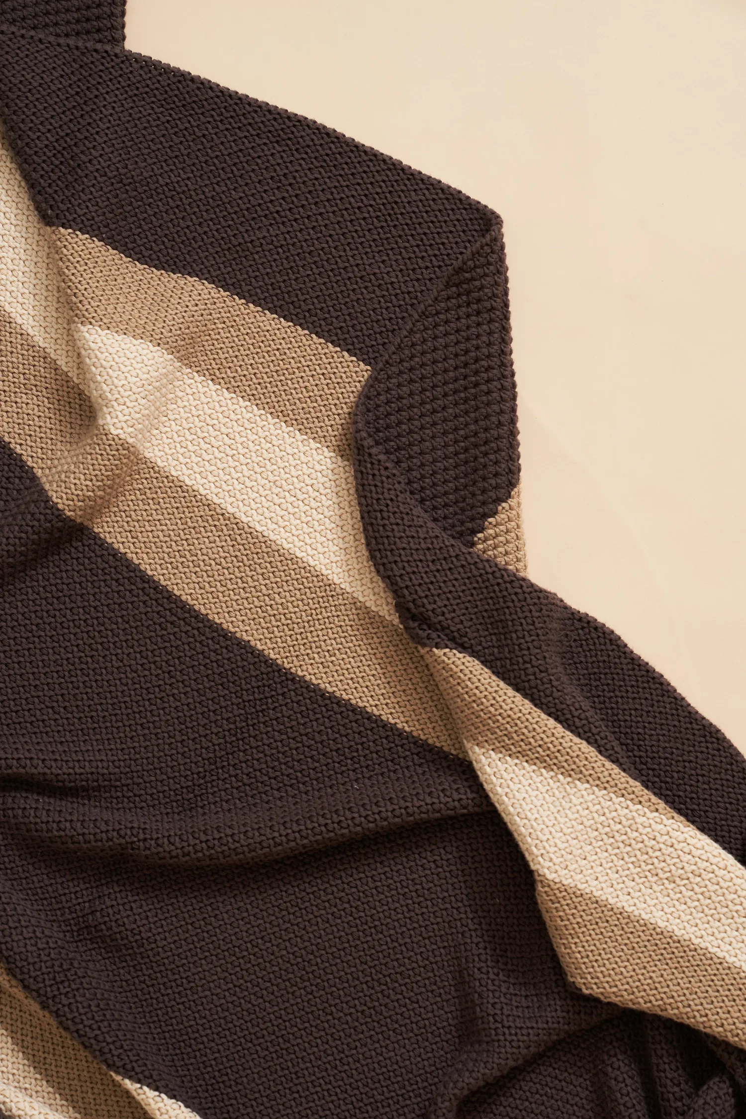 Close-up of a knitted textile with black, beige, and cream stripes, showing detailed texture and fabric.