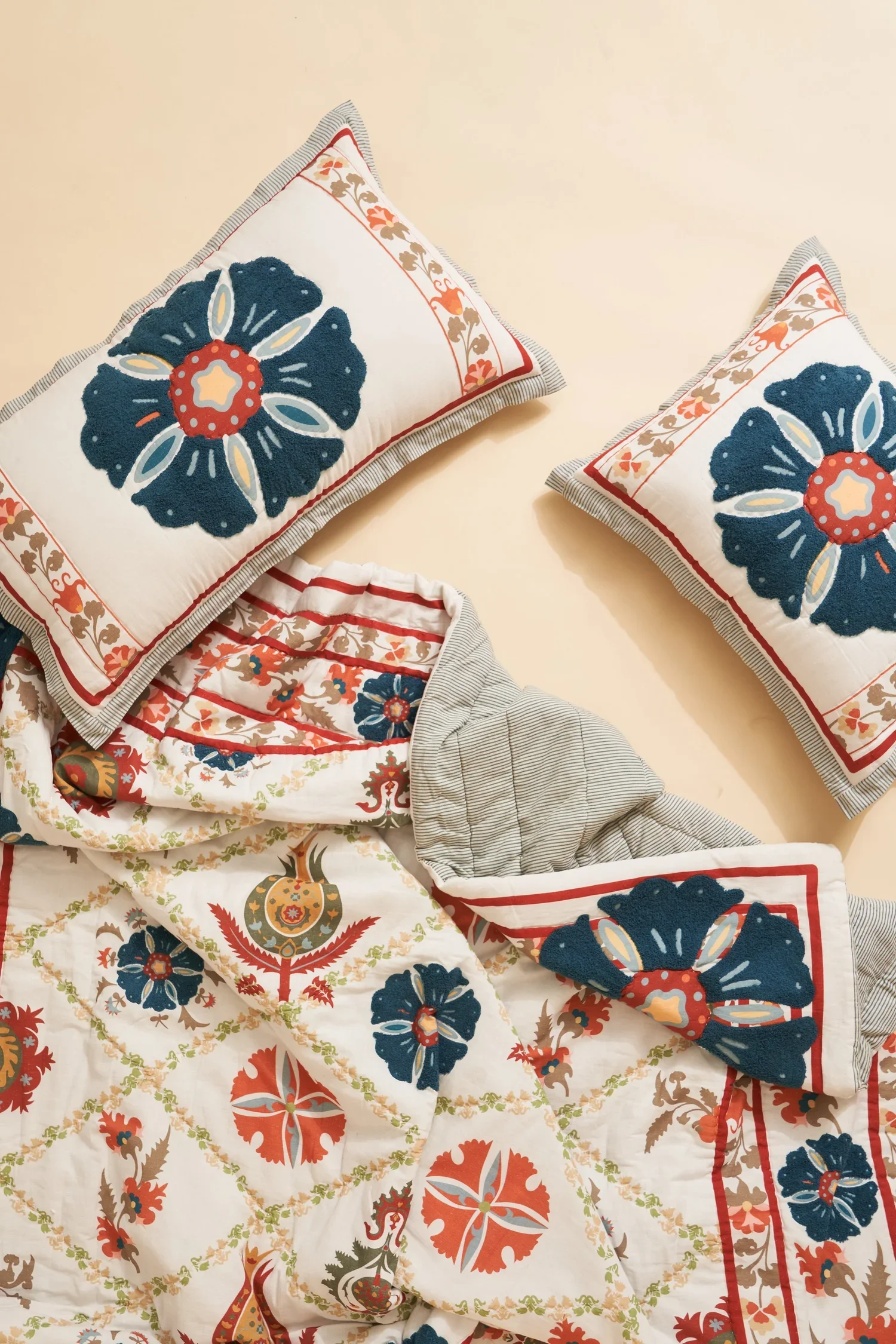Decorative pillows with bold floral and geometric patterns in red, navy, beige, and white, paired with a bedspread featuring matching designs.