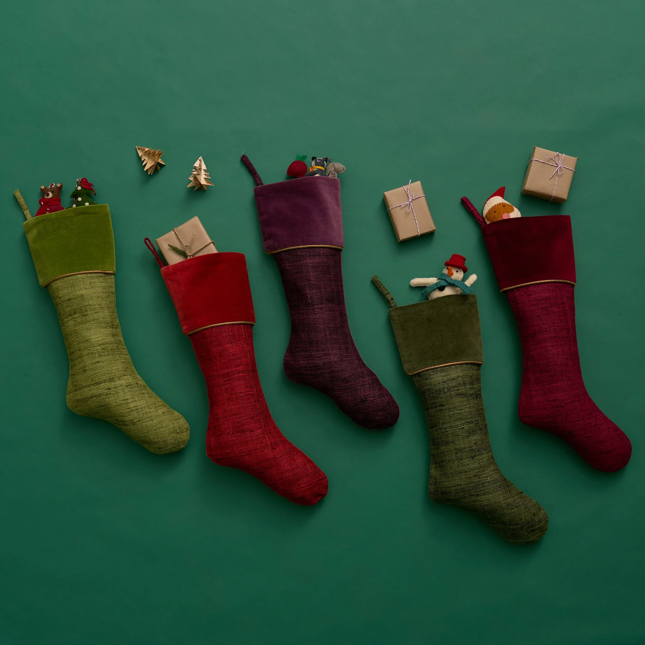 Christmas stockings filled with toys and presents on a green background with small decorative trees and gift boxes.