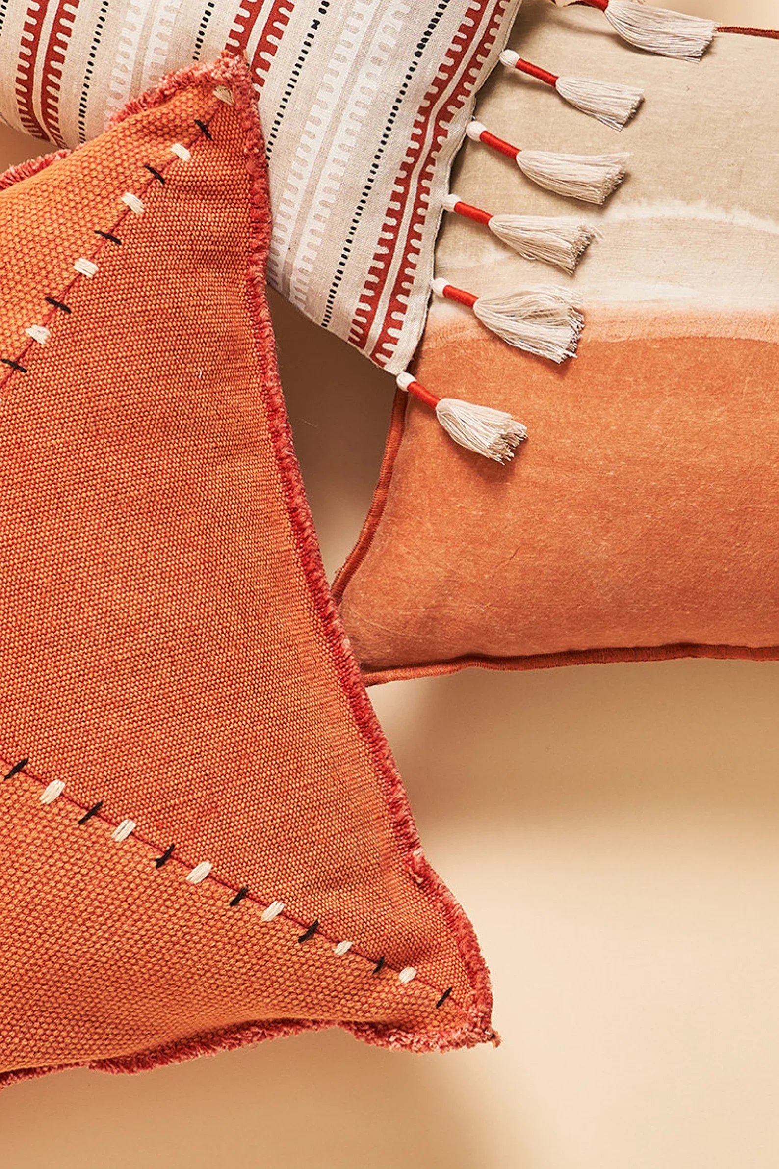 Close-up of two colorful, patterned throw pillows with tassels on a beige surface.