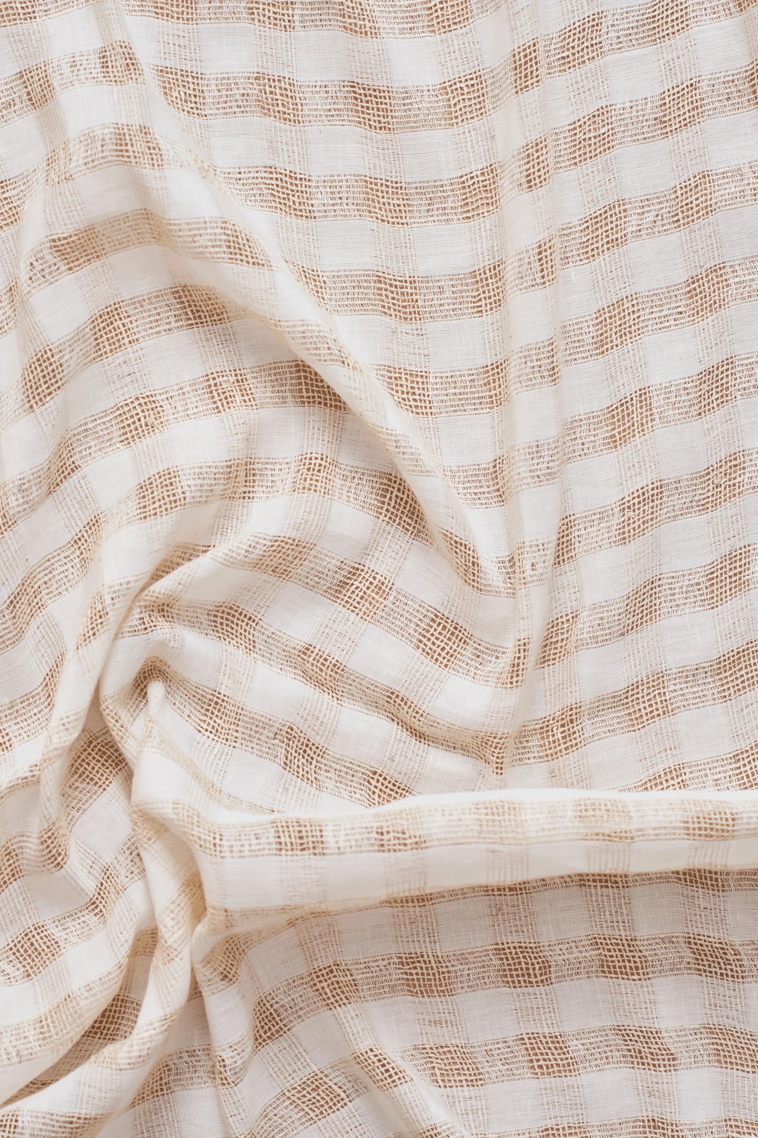 Close-up of a beige and white striped woven fabric with a textured pattern and some folds.