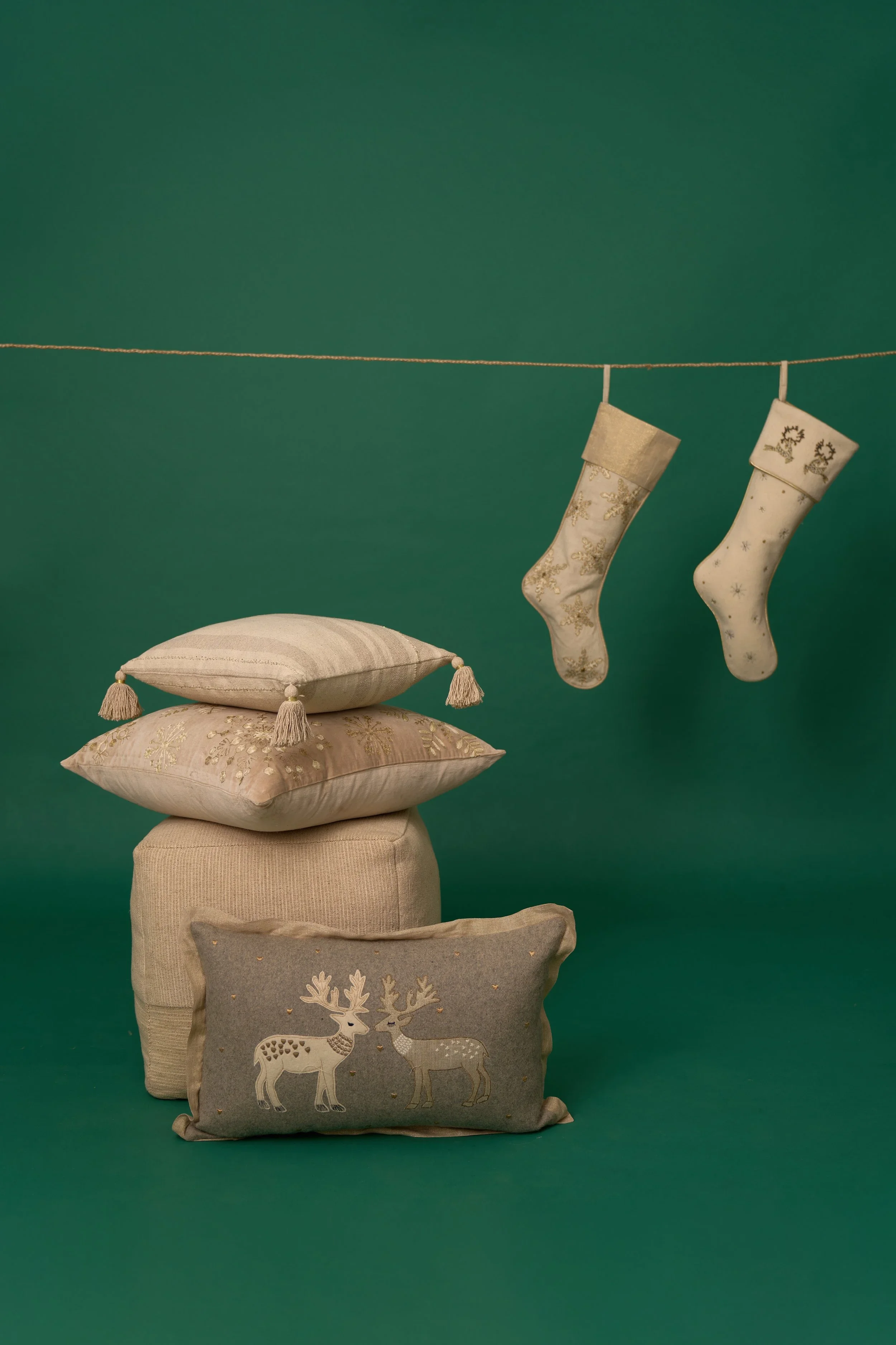 Christmas stocking decorations hanging from a string against a green background, with cushions and pillows stacked underneath.