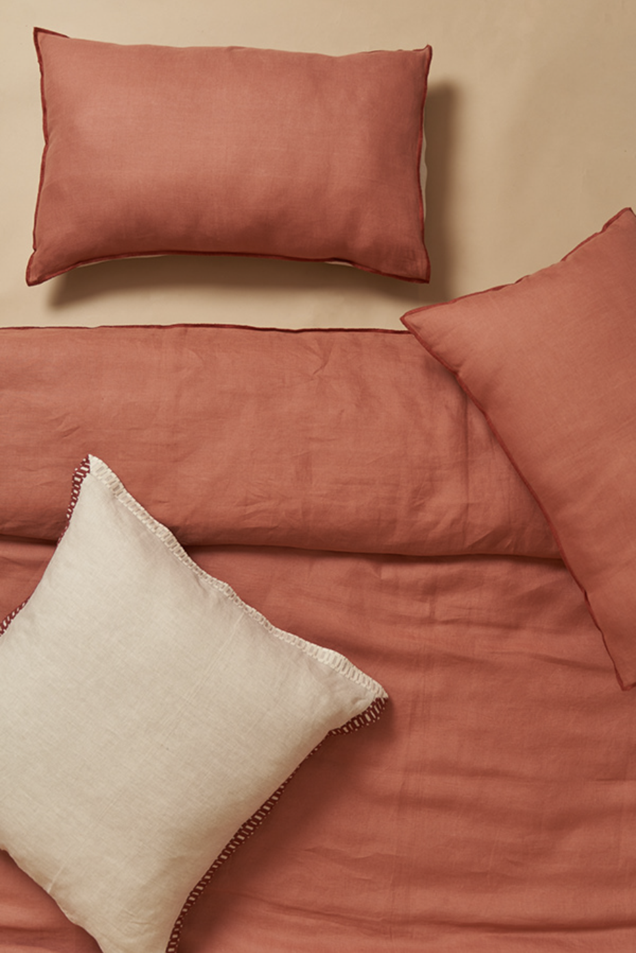 A set of coral pink pillowcases and bed sheets on a bed with a white decorative pillow with a fringed edge.