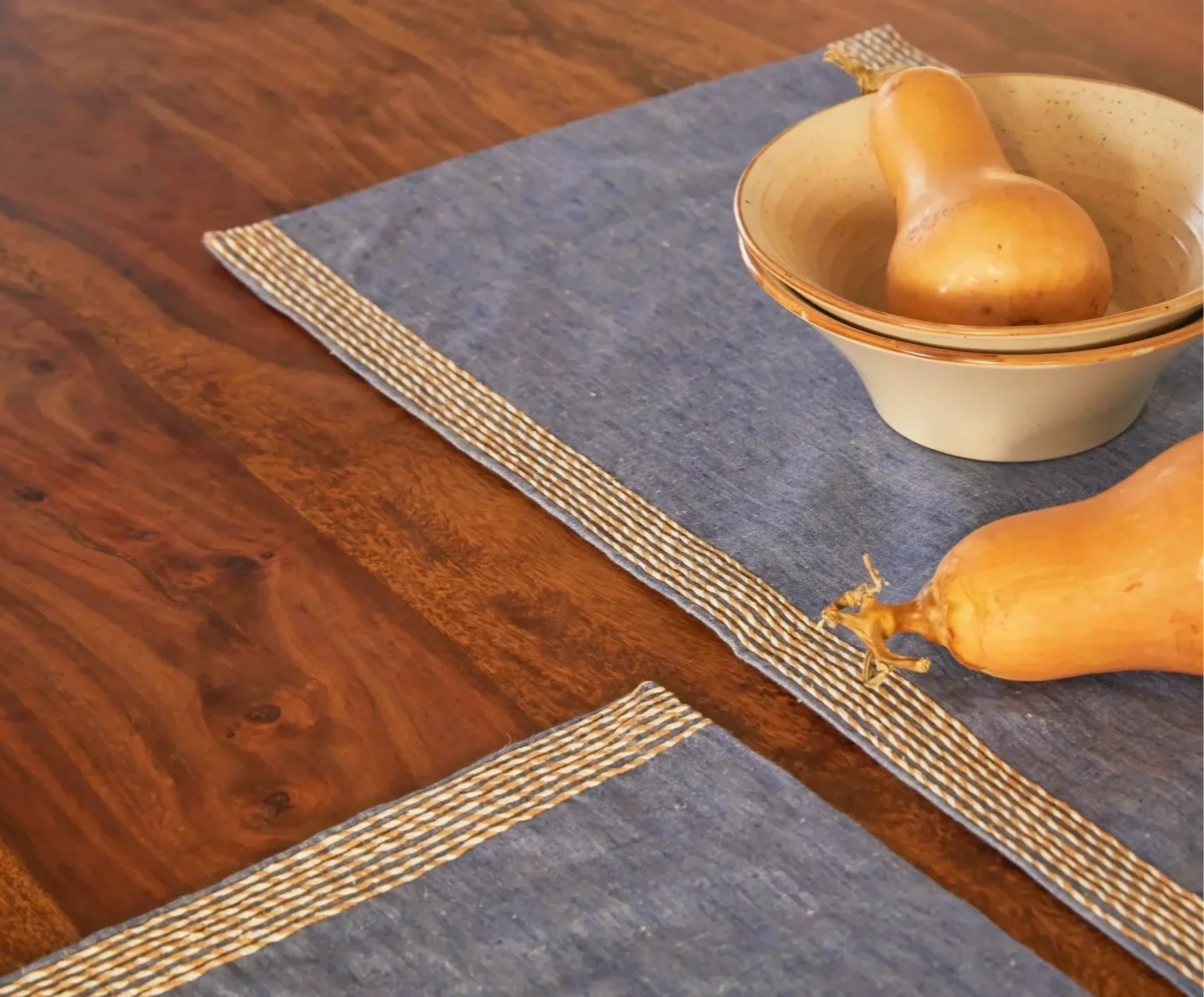 A wooden table with a dark blue cloth table runner bordered with a woven pattern, featuring a beige mortar and pestle and a partially peeled onion.