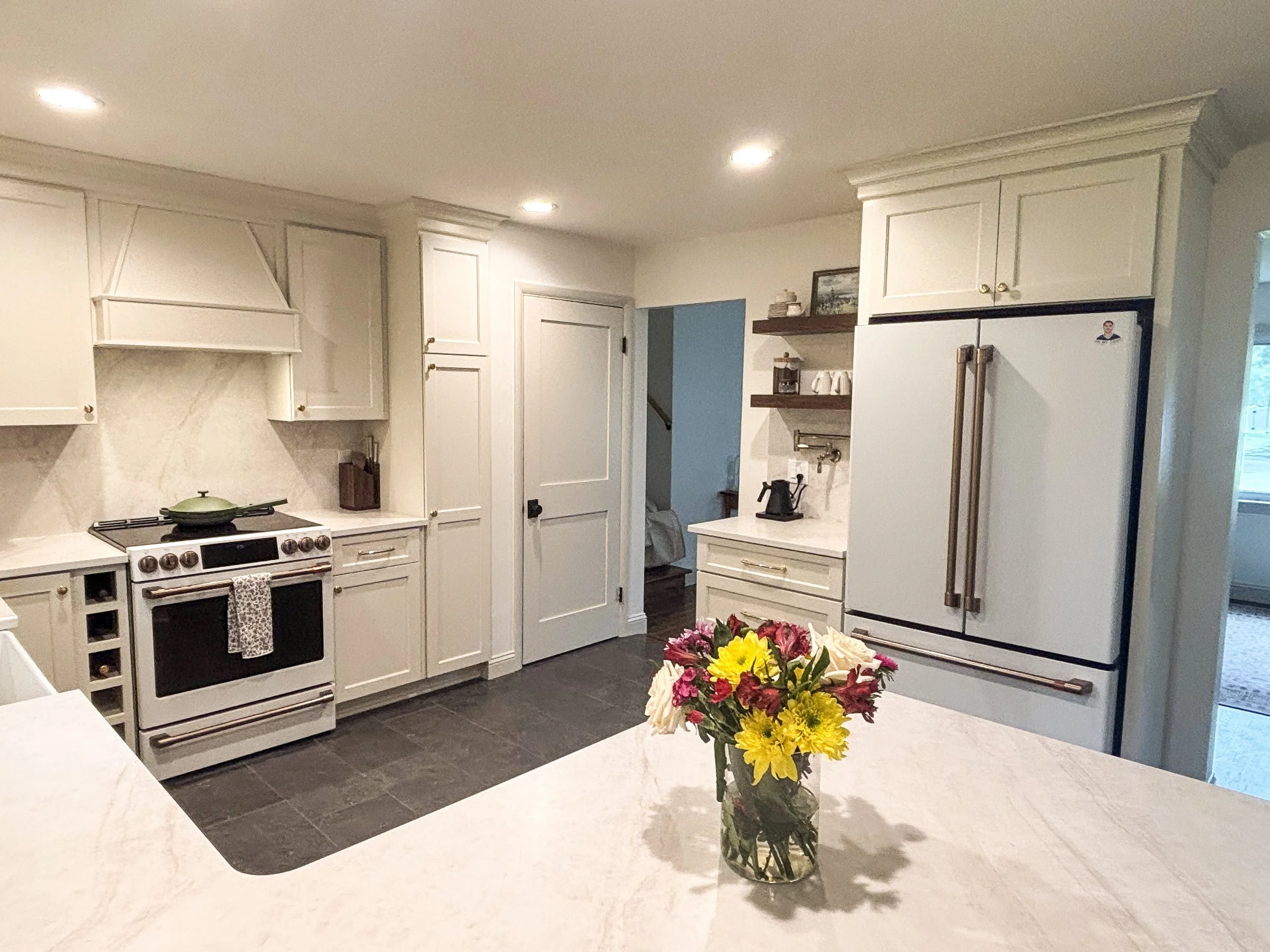 A kitchen with white cabinets, a stove, and a refrigerator. A bouquet of multicolored flowers on the counter.