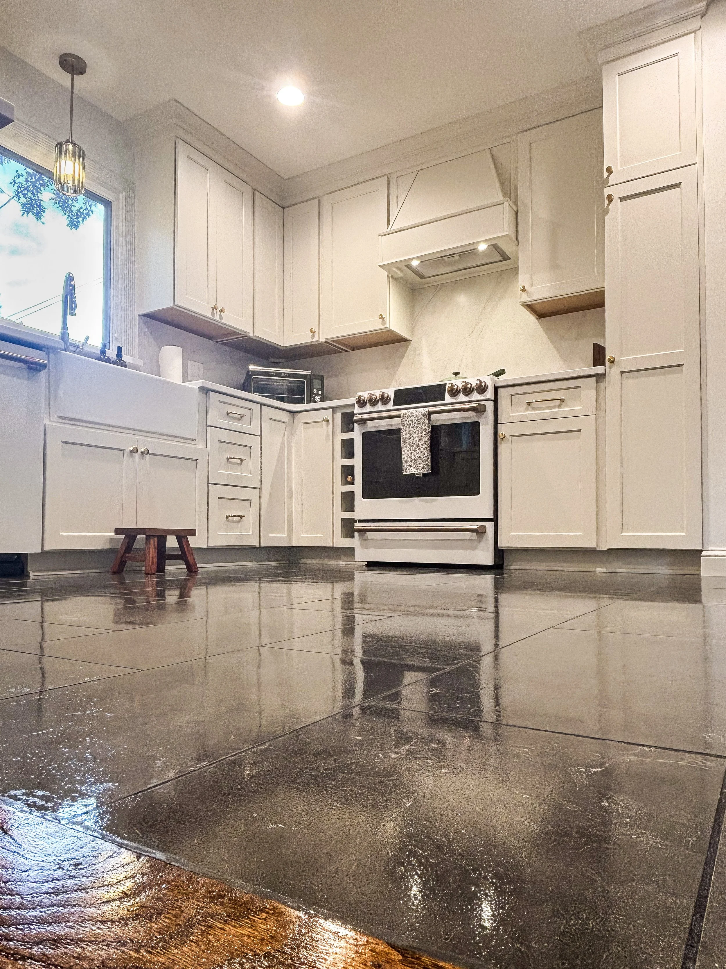 Kitchen with white cabinets, black stove, window with blue sky outside, and dark polished concrete floor.