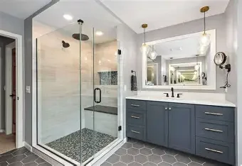 Modern bathroom with a glass-enclosed shower and blue vanity with white countertop, mirror, and hanging light fixtures.