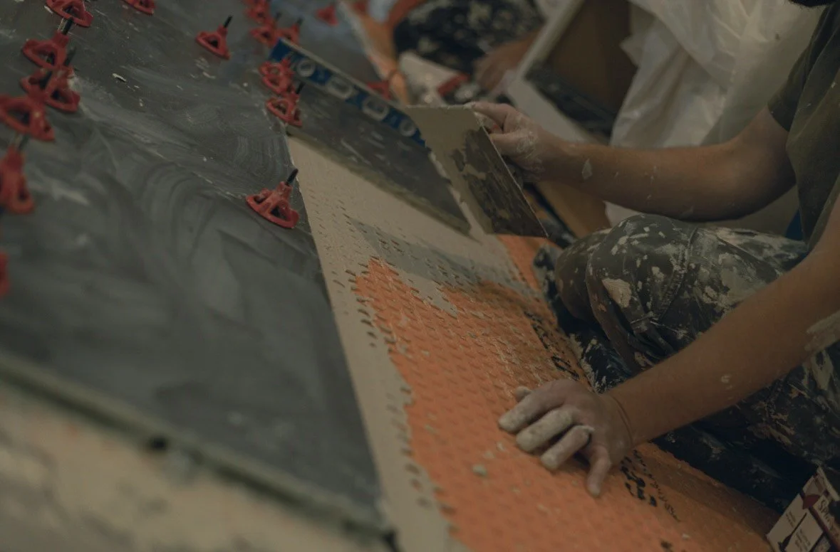 Close-up of a person installing orange and gray floor tiles, with red spacers, on a black surface.