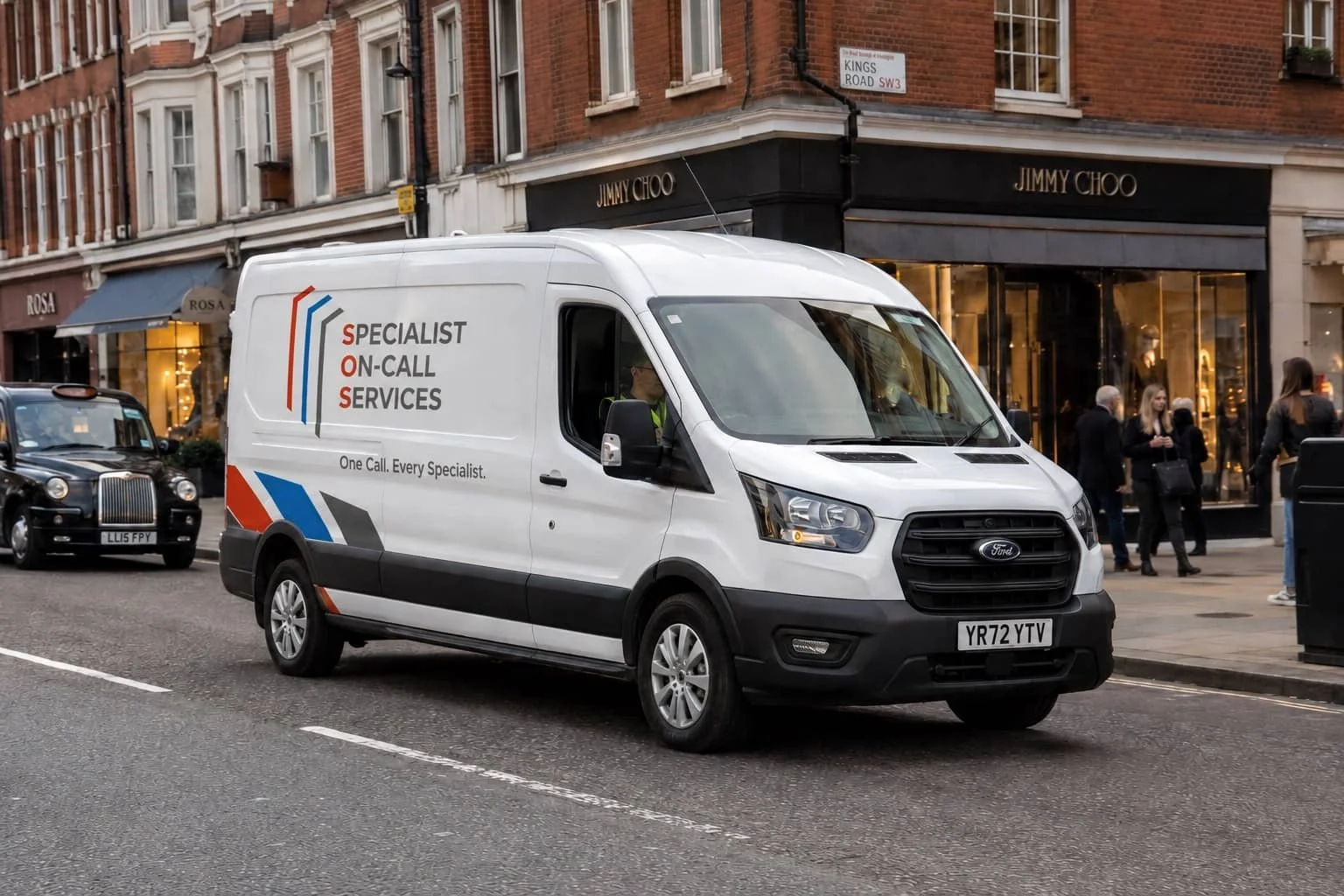 White service van with 'Specialist On-Call Services' logo and slogan on a city street in front of retail stores, with pedestrians nearby.