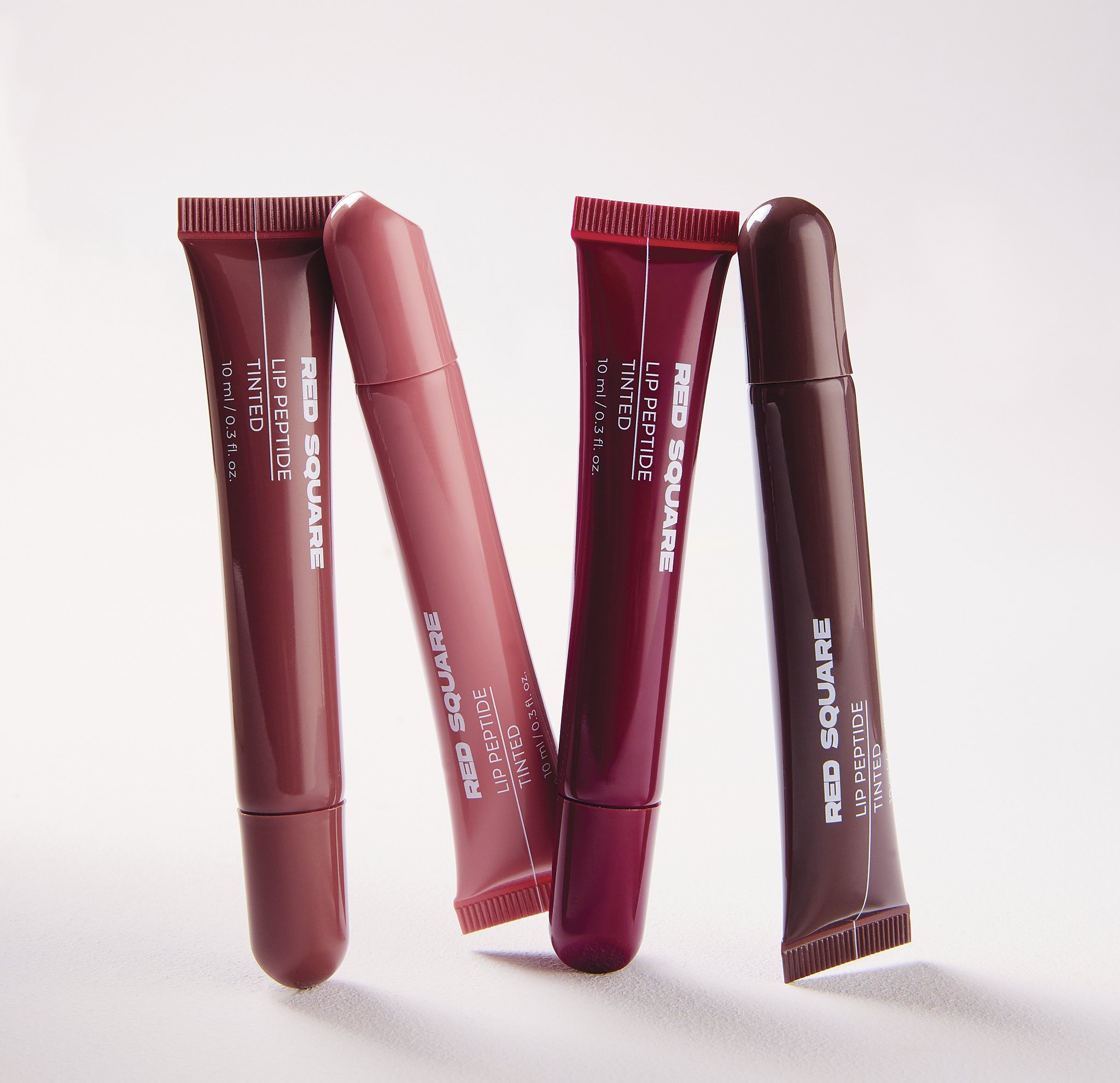 Four tubes of liquid lip tint in shades of pink and red, standing upright on a white surface with a plain white background.
