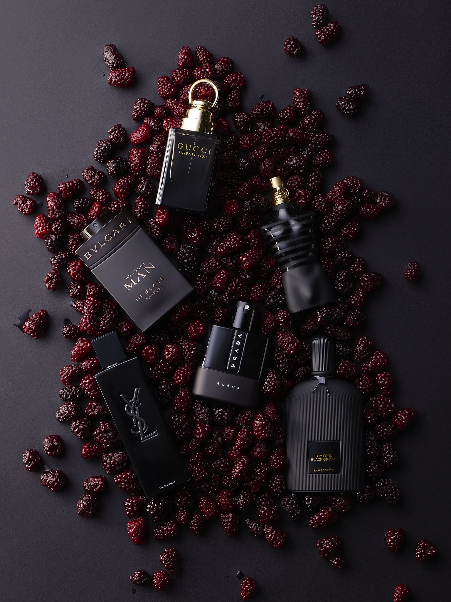 Collection of luxury perfume bottles, surrounded by fresh blackberries on a dark background.