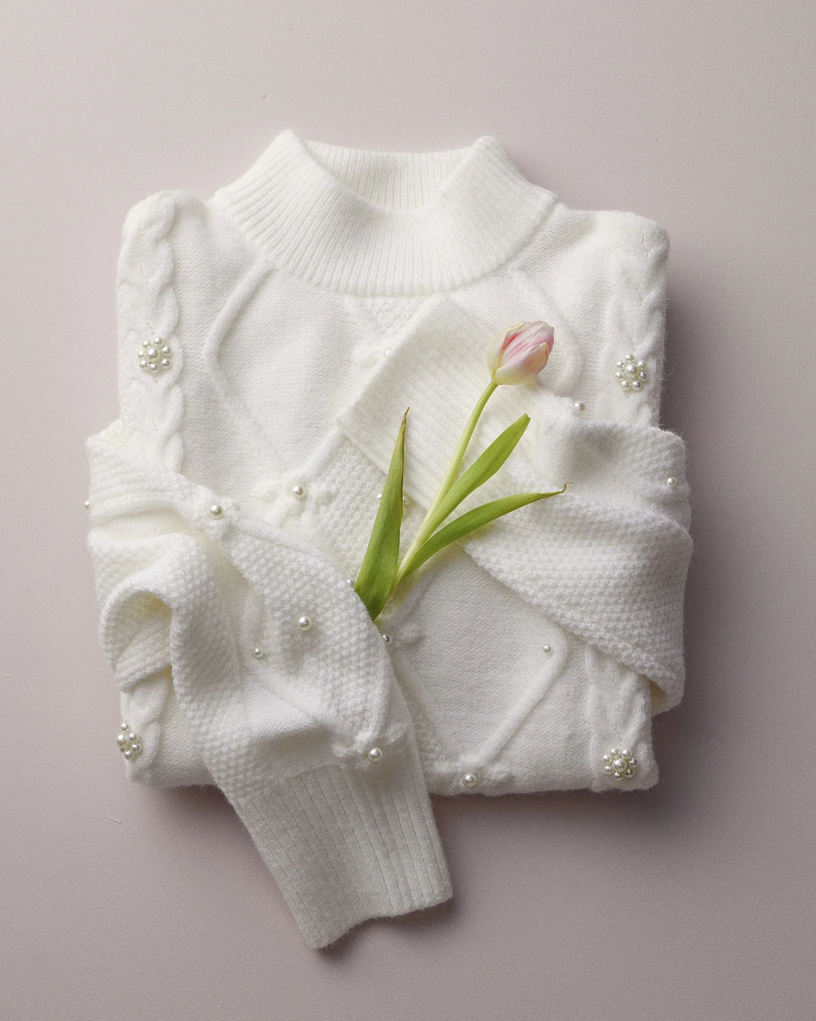 White knitted sweater with pearl embellishments and a pink tulip flower on a light-colored background.