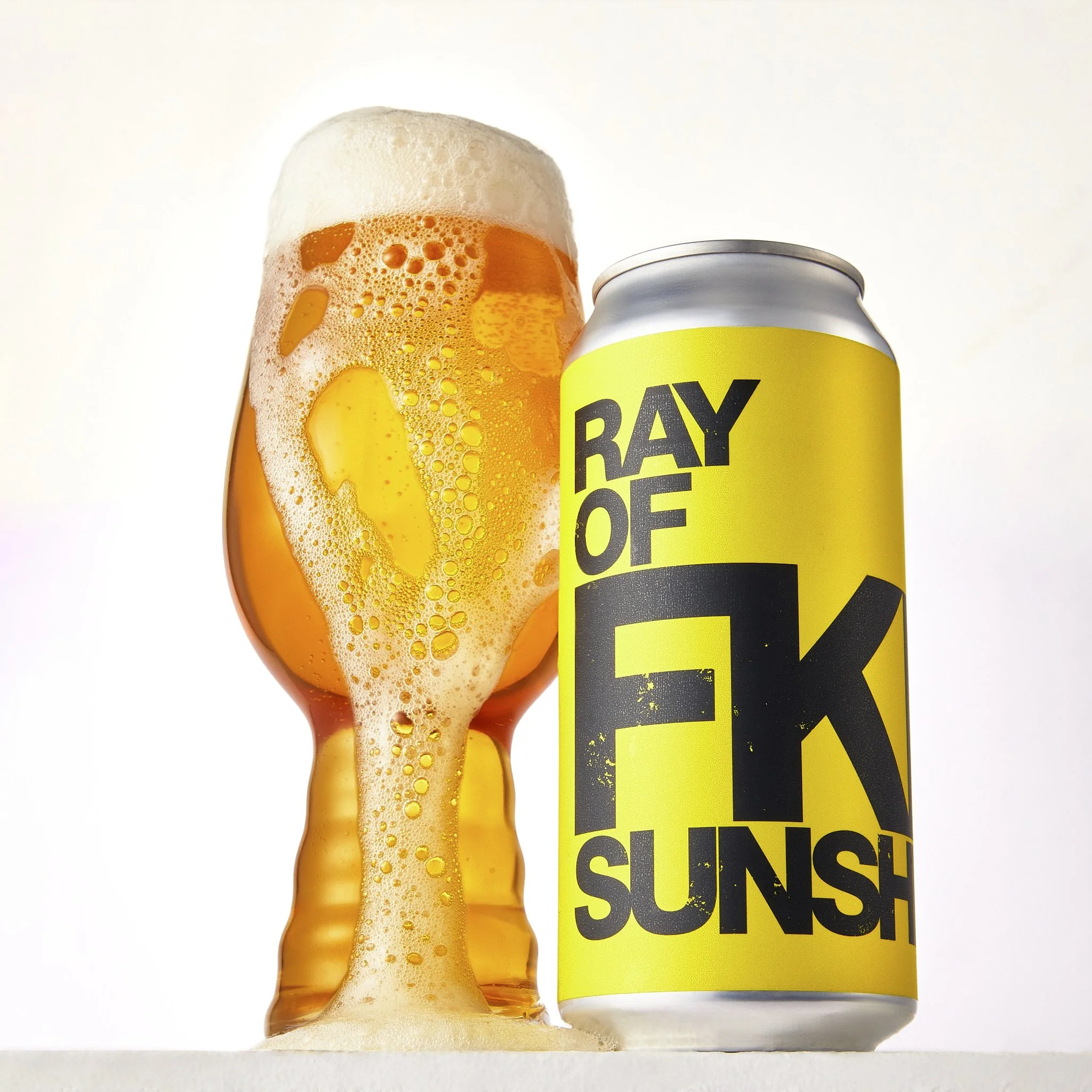 Close-up of a beer can labeled 'RAY of FKN Siunshine' next to a tall glass filled with orange beer topped with foam.