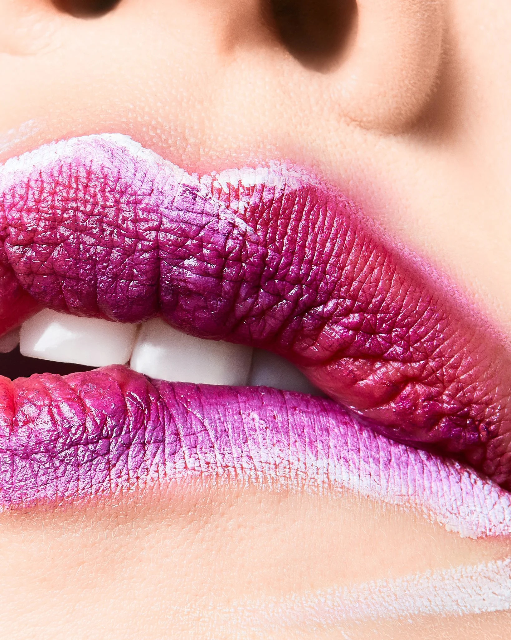 Close-up image of lips with purple lipstick and white frosted upper lip, lips partially open revealing teeth and a tongue with pink and purple lipstick.