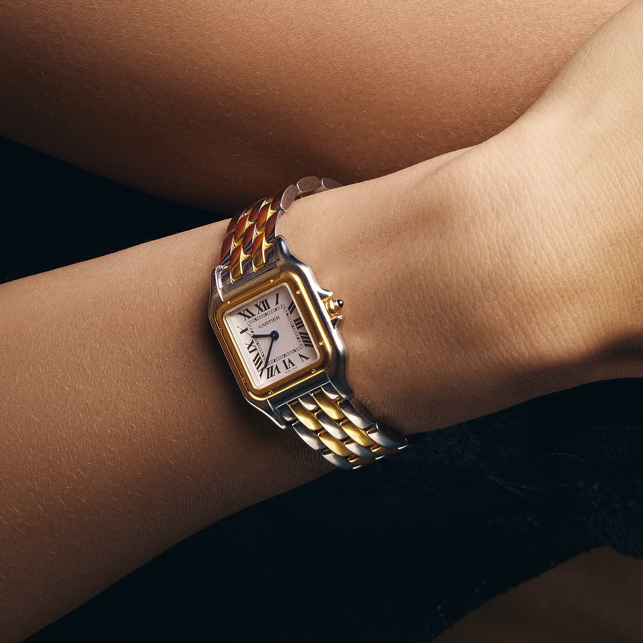 Close-up of a person's wrist wearing a two-tone gold and silver Cartier watch on a dark background with a bracelet.