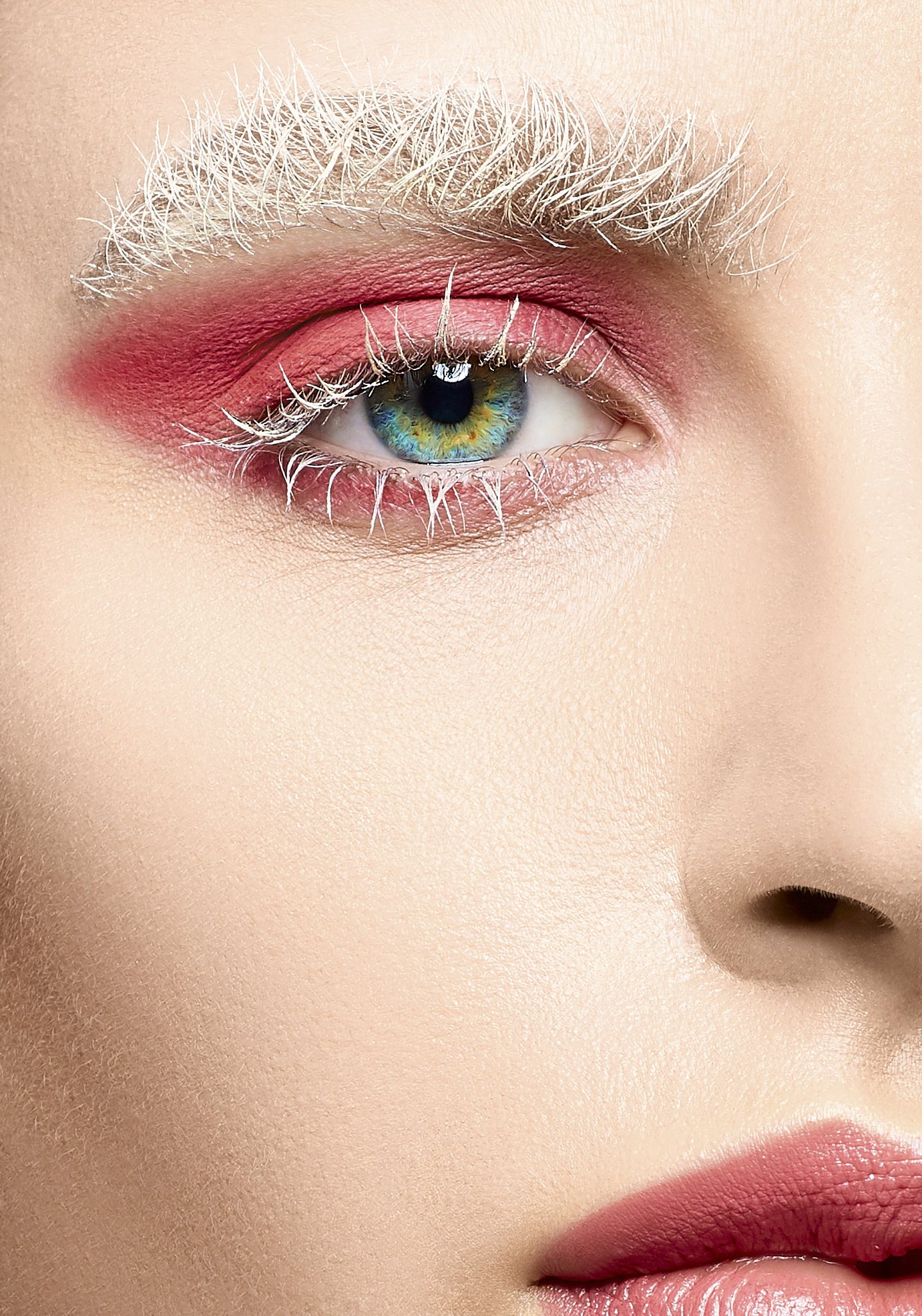 Close-up of a person's eye with vibrant blue and green iris, pink and red eye makeup, and white eyelashes, with visible skin texture.