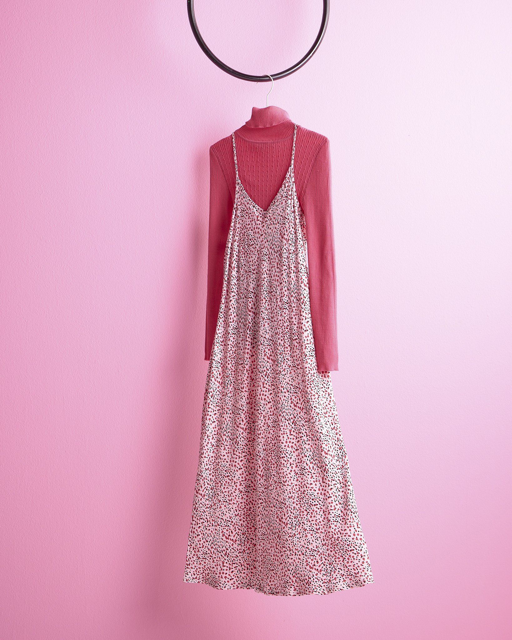 Legit pink long-sleeve turtleneck sweater dress with a leopard print slip dress hanging over it, on a black hanger against a pink wall.