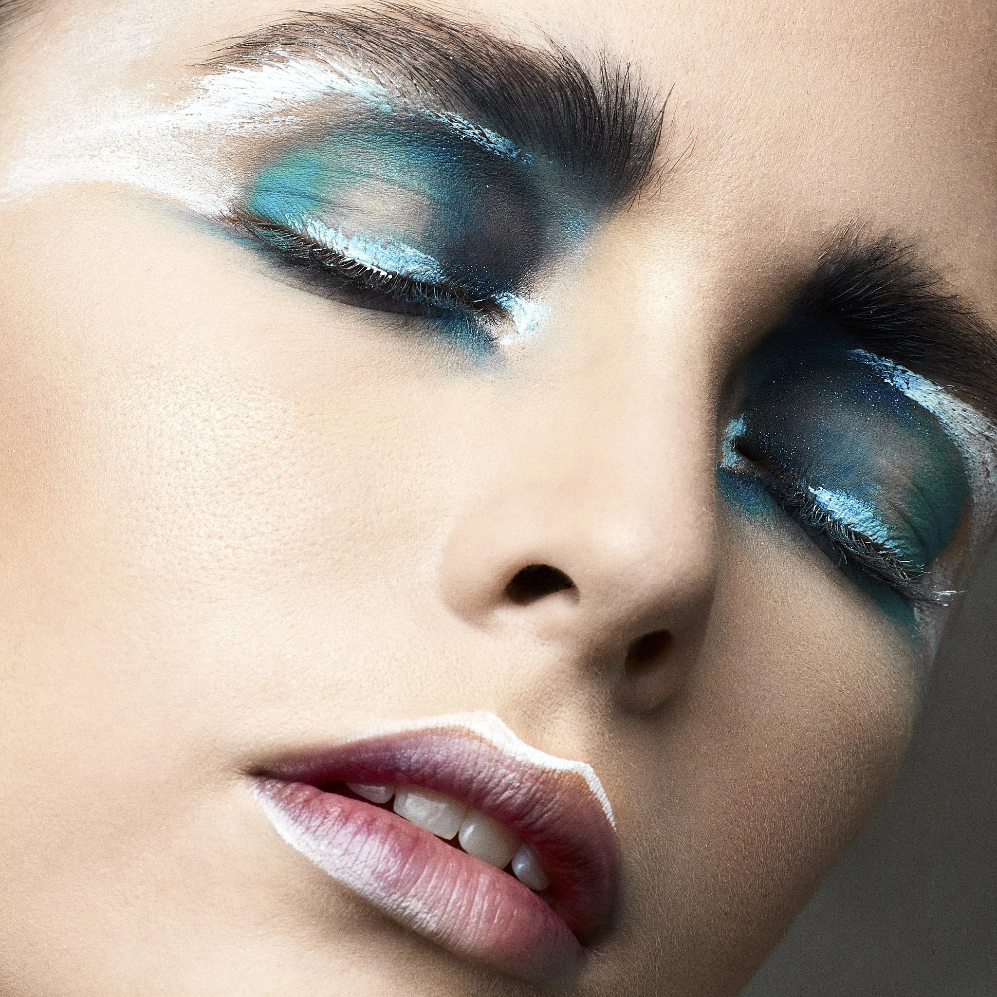 Close-up of a person’s closed eye with vibrant blue and black eyeshadow, and long curled eyelashes.