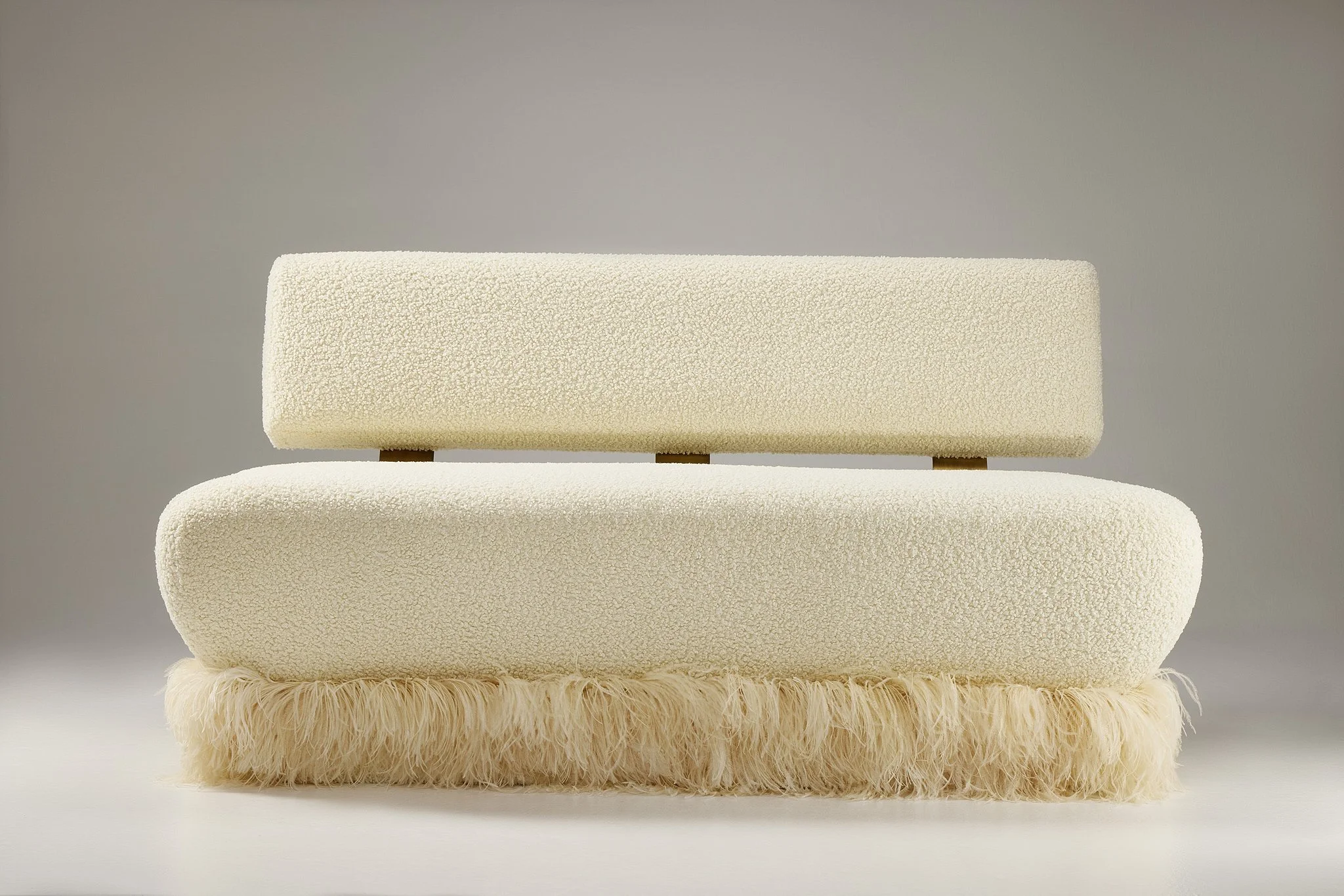 A white flocked couch with soft and textured surfaces, fringed with ostrich feathers arranged on a surface against a plain background.