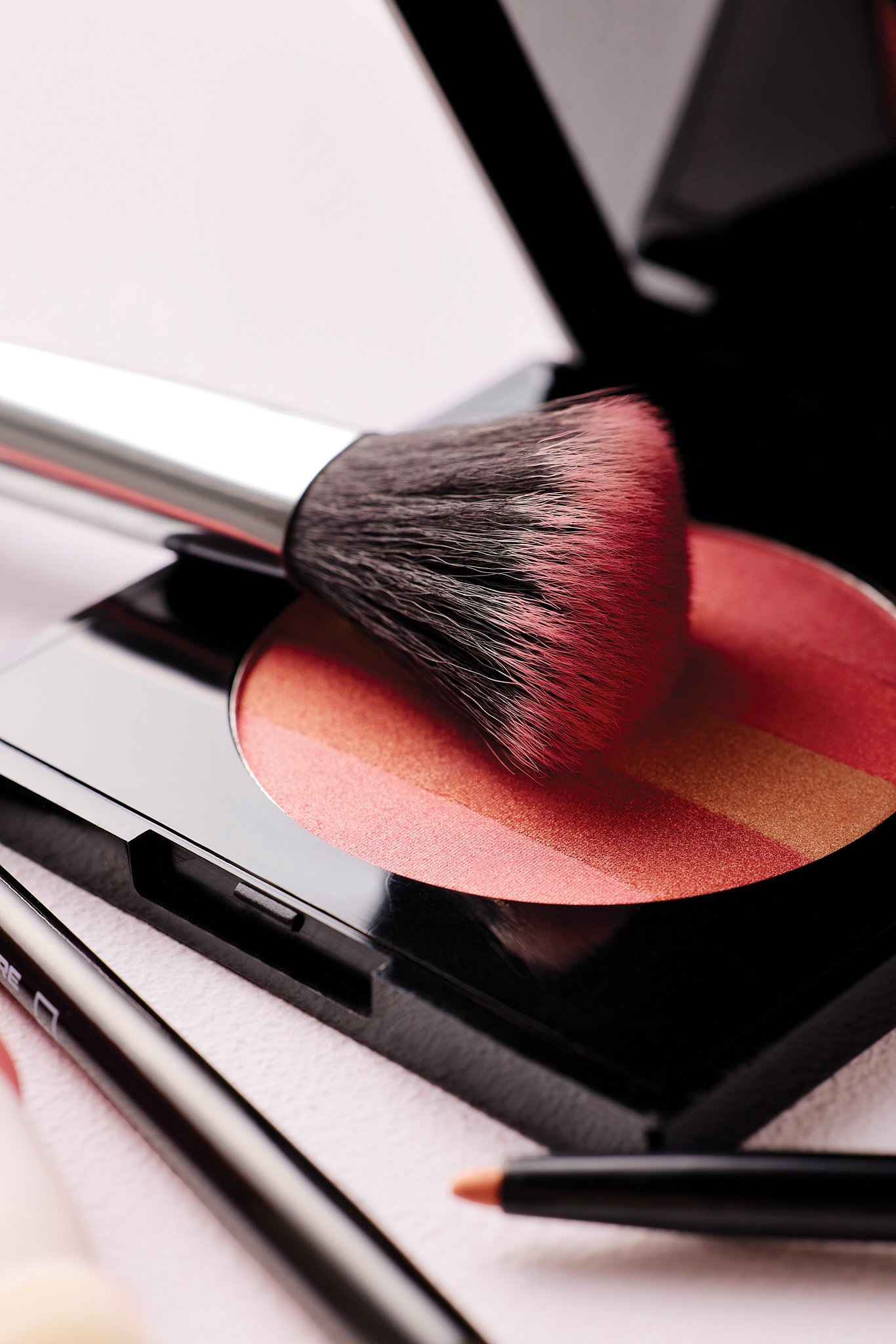 A makeup brush resting on a peach-colored eyeshadow with a makeup pencil nearby, all placed on a makeup palette.