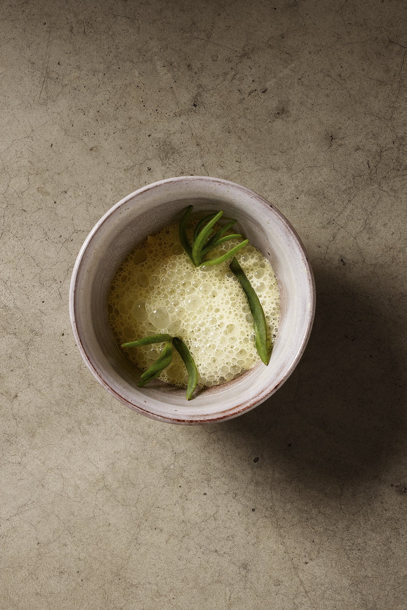 A ceramic cup containing a muscle dish covered in a foam with green succulent  pieces inside, placed on a concrete surface.