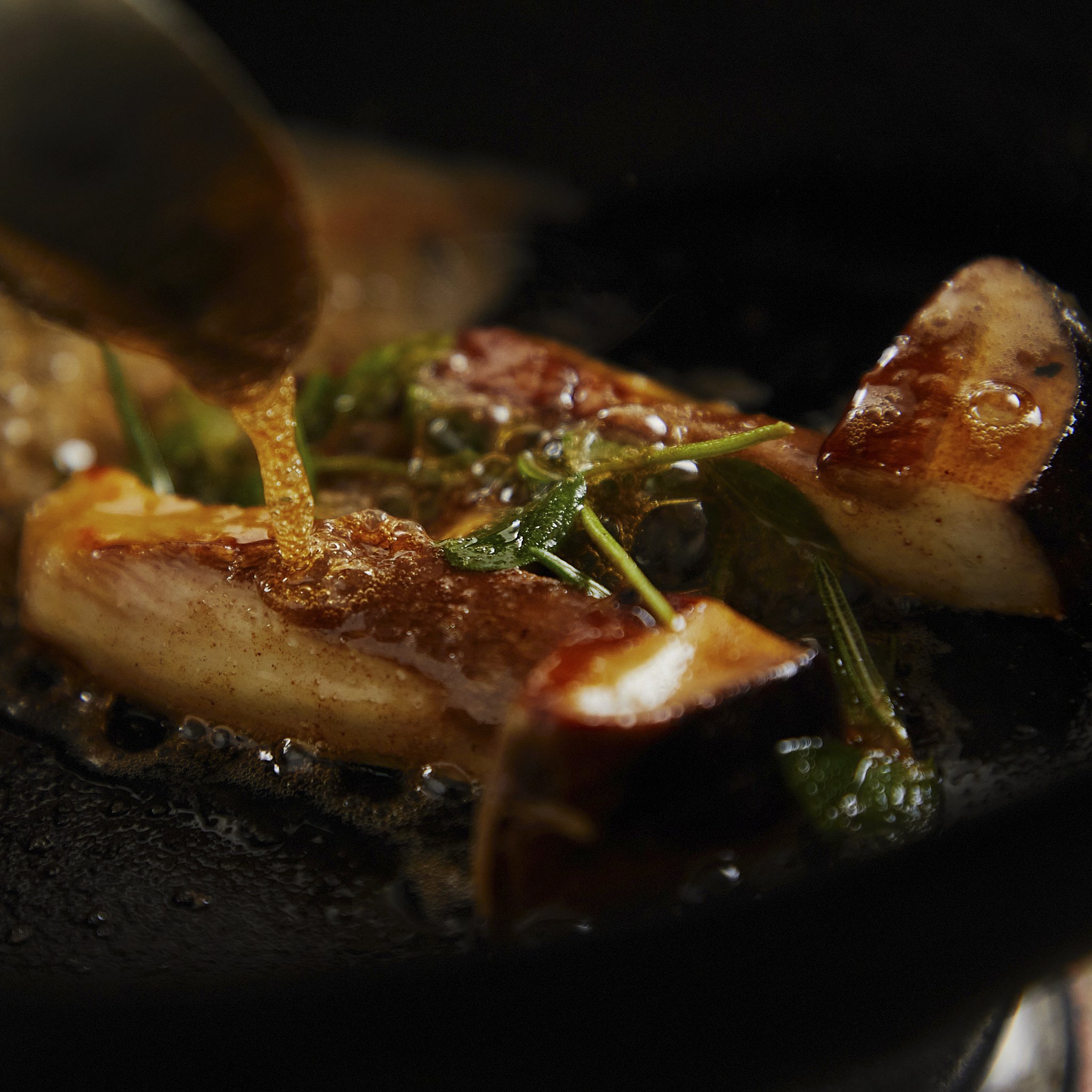 Close-up of mushrooms sautéing in a pan filled with butter with some greenery.