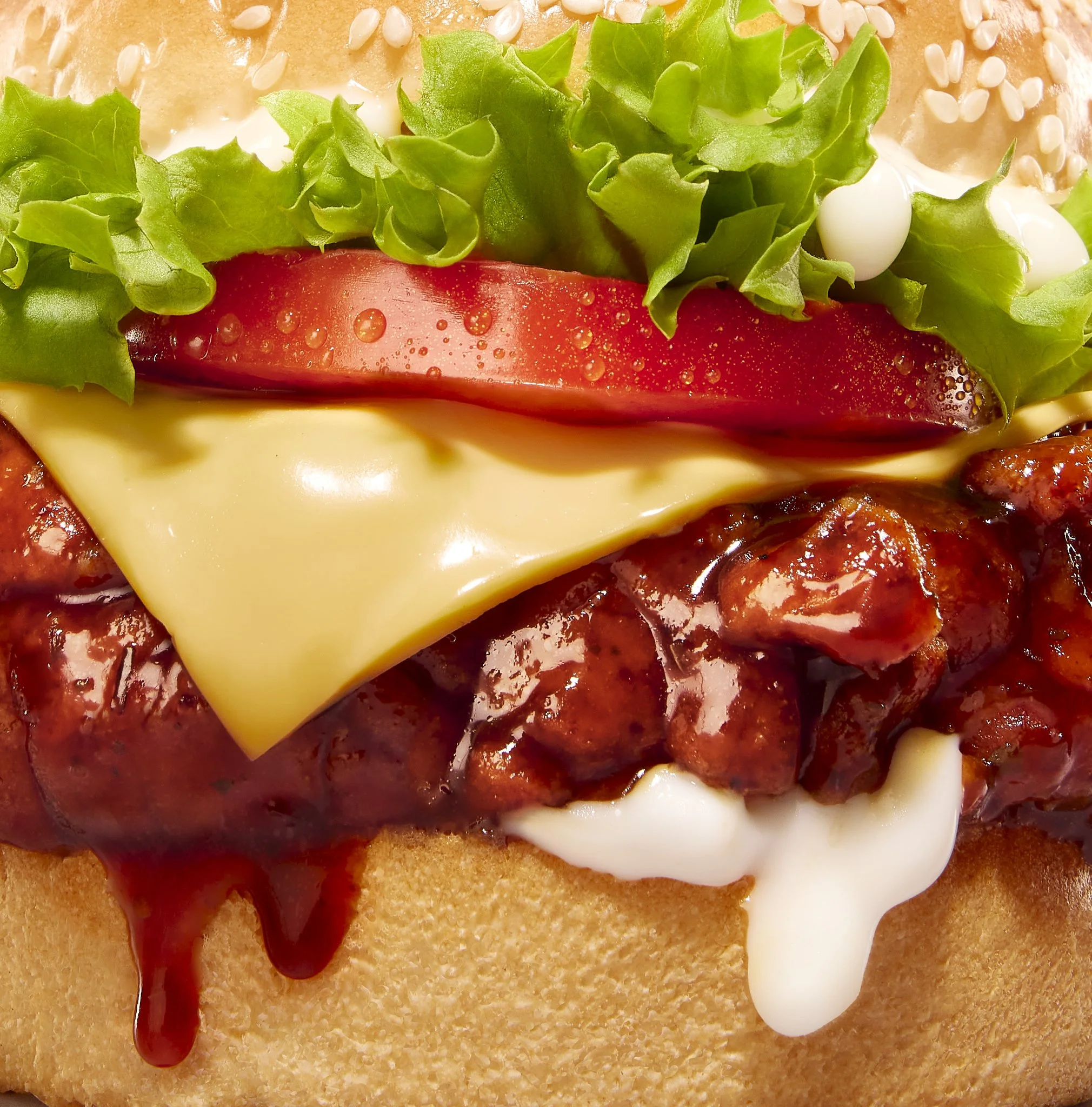 Close-up of a burger with toppings including lettuce, tomato, cheese, barbecue sauce, and mayonnaise on a bun.