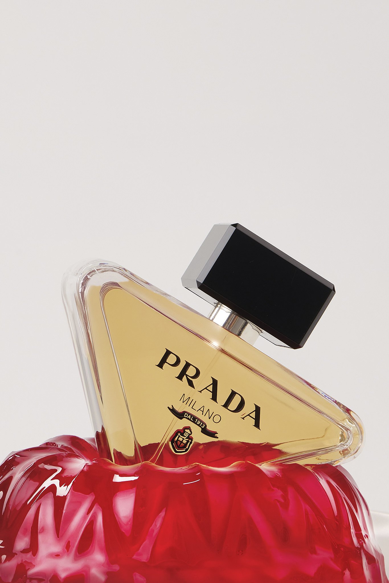 Close-up of a Prada Milan perfume bottle resting on red roses, with a black spray cap.