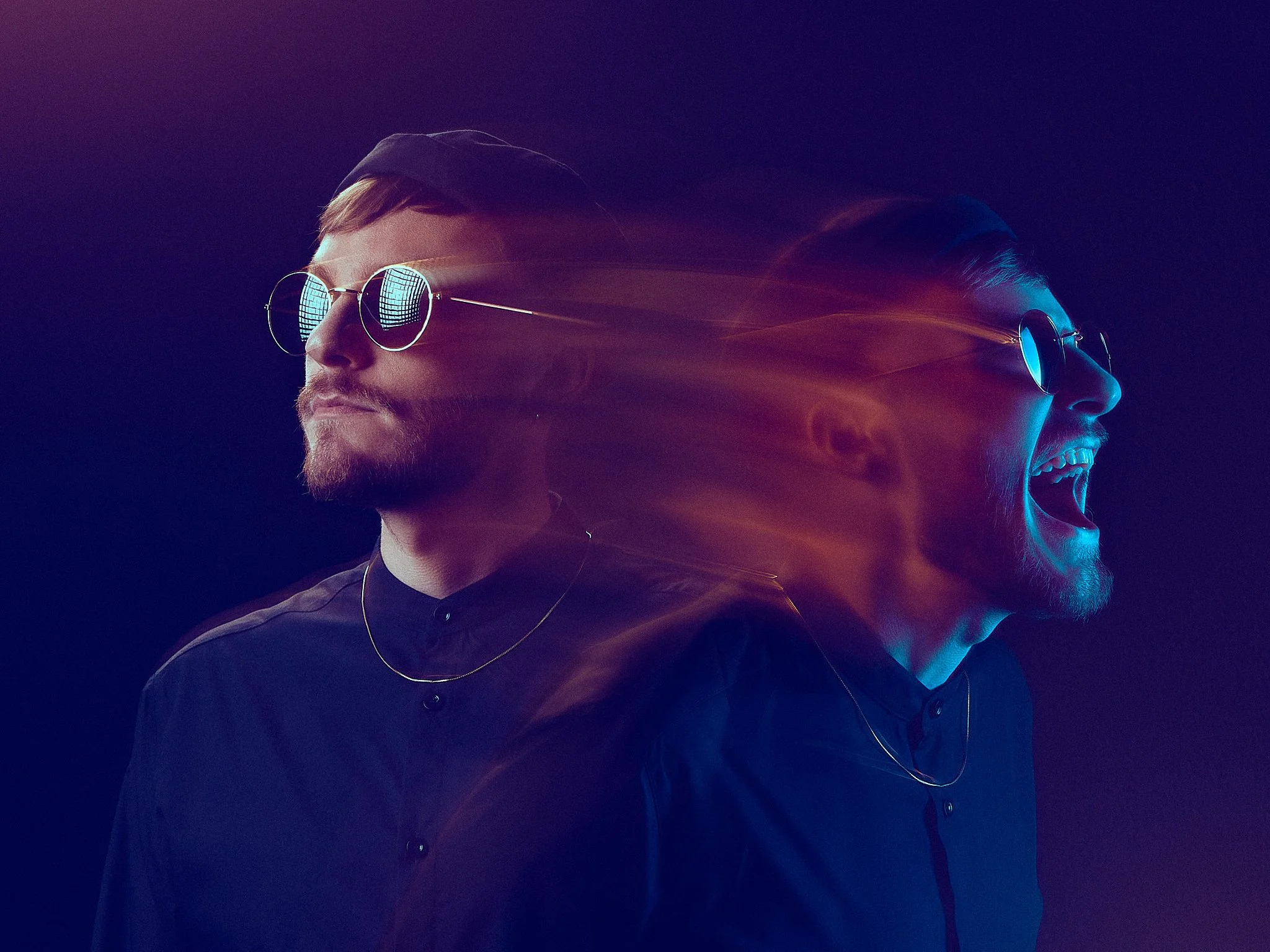 A single frame long exposure image of a man with a short beard and sunglasses looking to the side, with blue and purple light effects and a second face of him yelling or singing, blending into the background.  no photoshop
