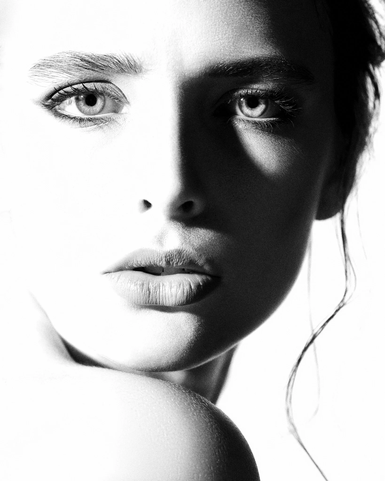 Close-up black and white photo of a woman's face showing her eyes, nose, and lips, with high contrast lighting.