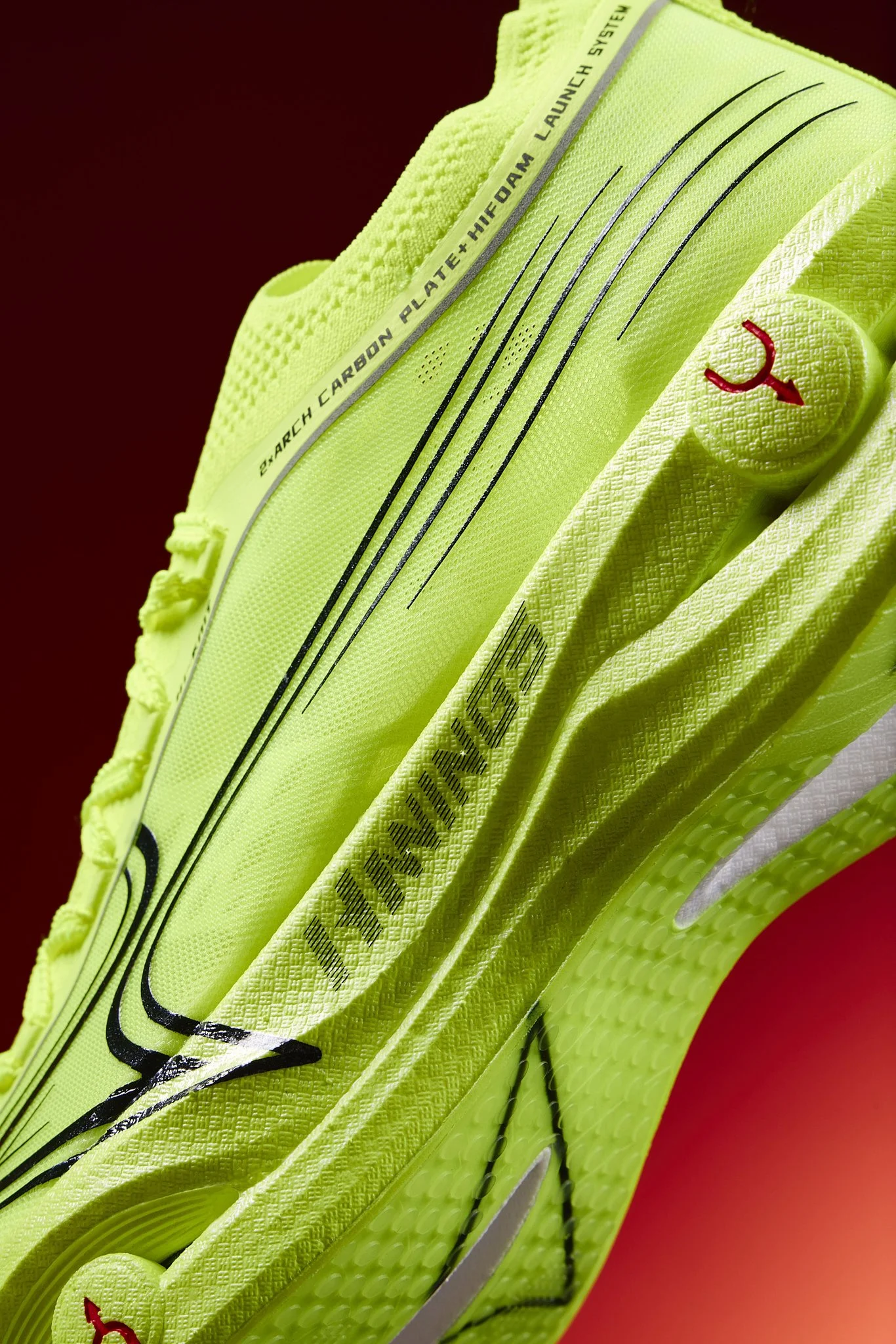 Close-up of a neon yellow athletic running shoe with black accents and red logo, set against a red background.