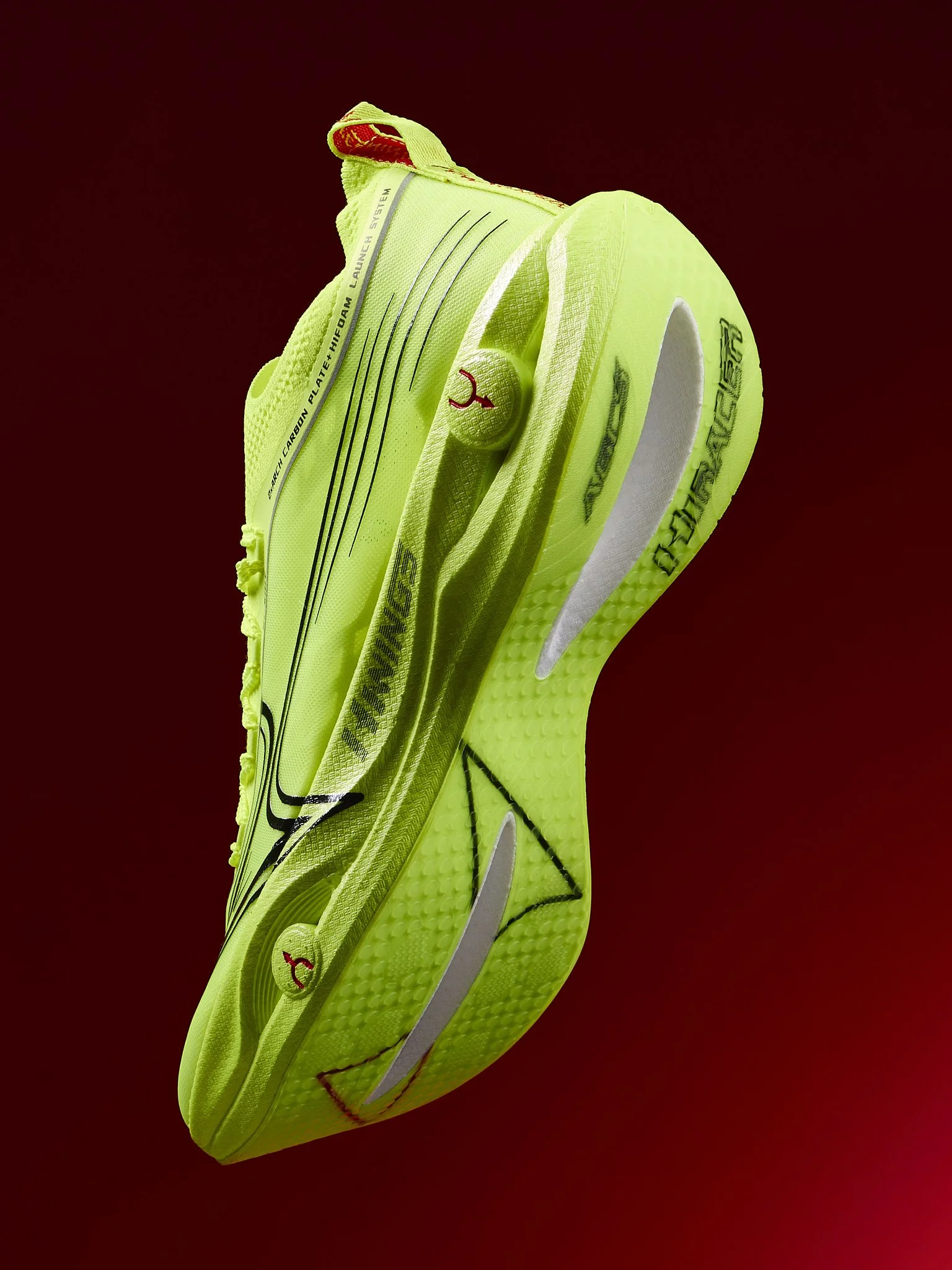 A bright yellow-green athletic running shoe with black and red accents, floating against a dark red background.