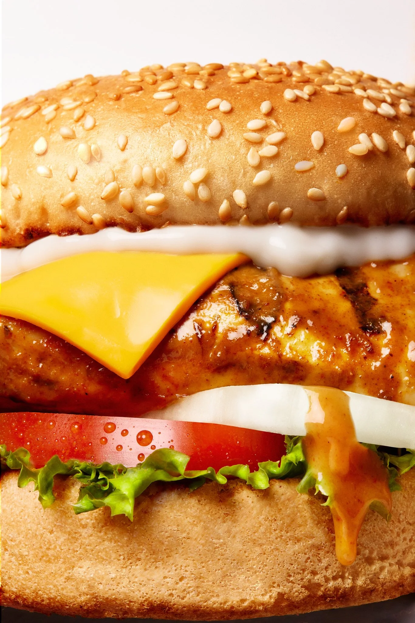 Close-up image of a cheeseburger with sesame seed bun, lettuce, tomato, cheese, and burger patty with sauce, with a small piece of lettuce and tomato at the bottom.
