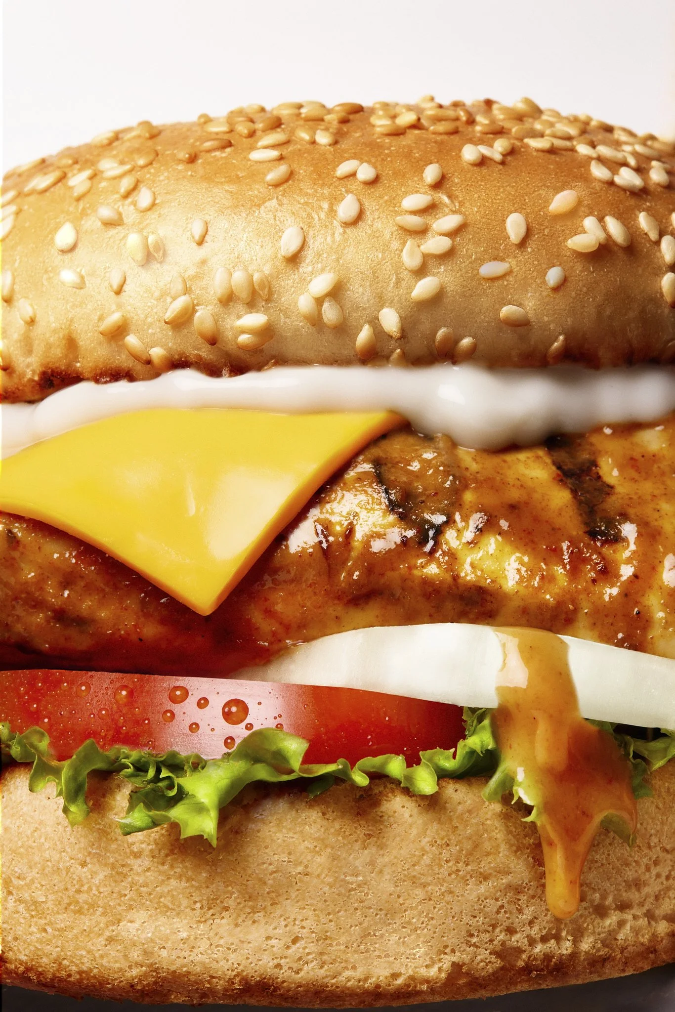Close-up image of a cheese burger with a sesame seed bun, lettuce, tomato, melted cheese, and sauce.