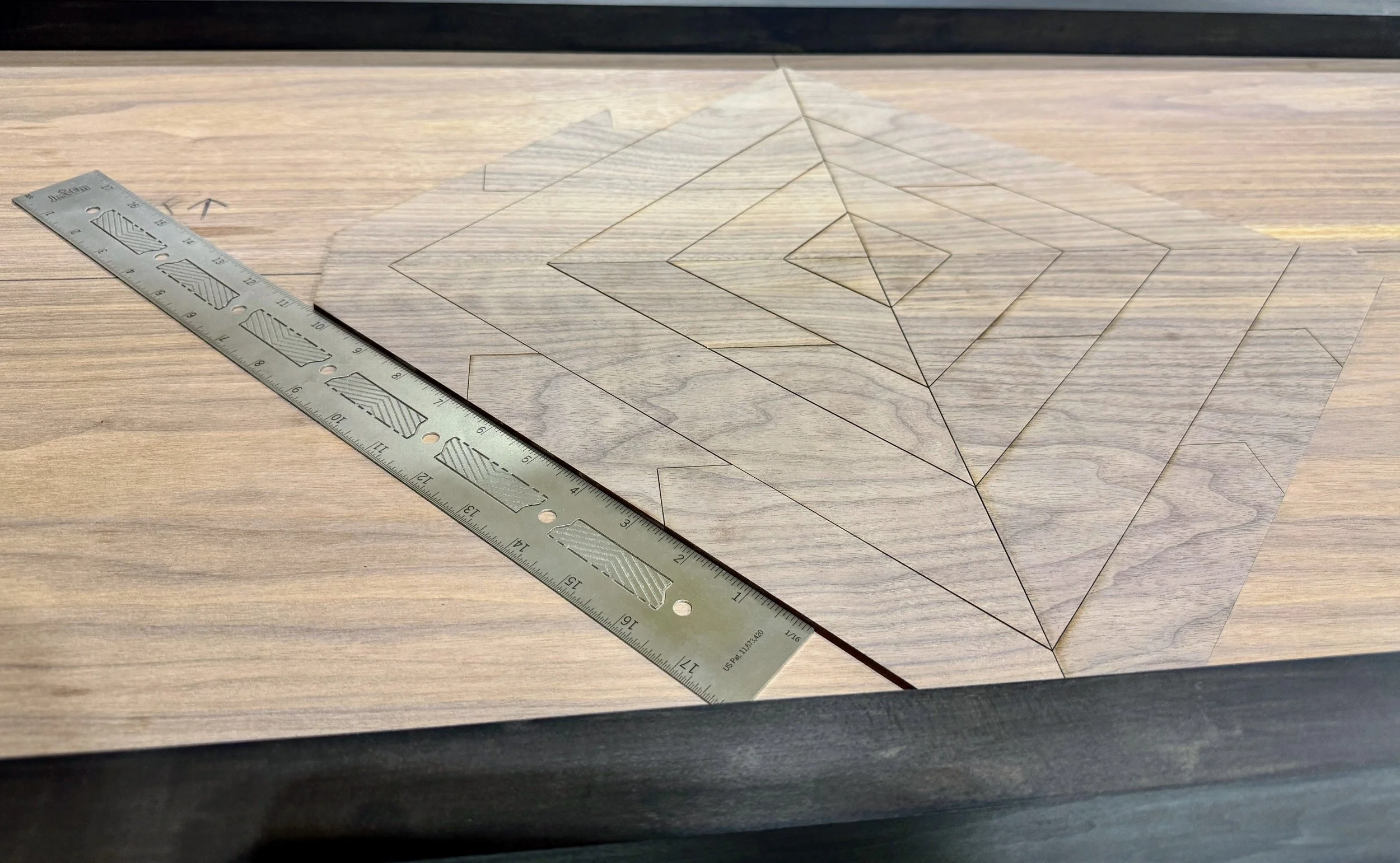 A wooden surface with a geometric design drawn on a piece of transparent tracing paper, a metal ruler placed nearby for measurement, with the background being a darker wooden border.