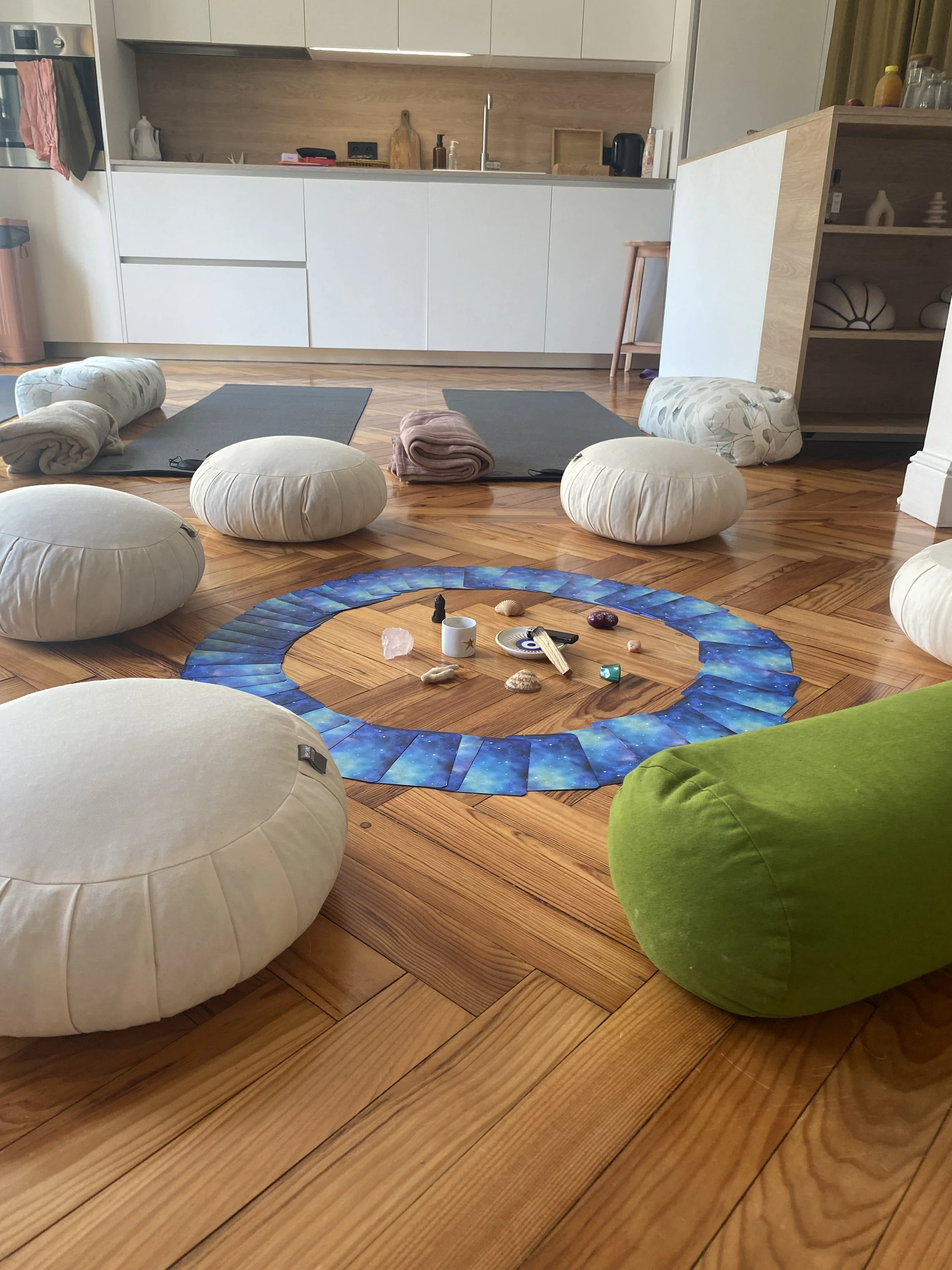Une pièce aménagée pour la pratique du yoga avec des coussins, des tapis, et des objets de méditation disposés en rond sur un sol en bois.