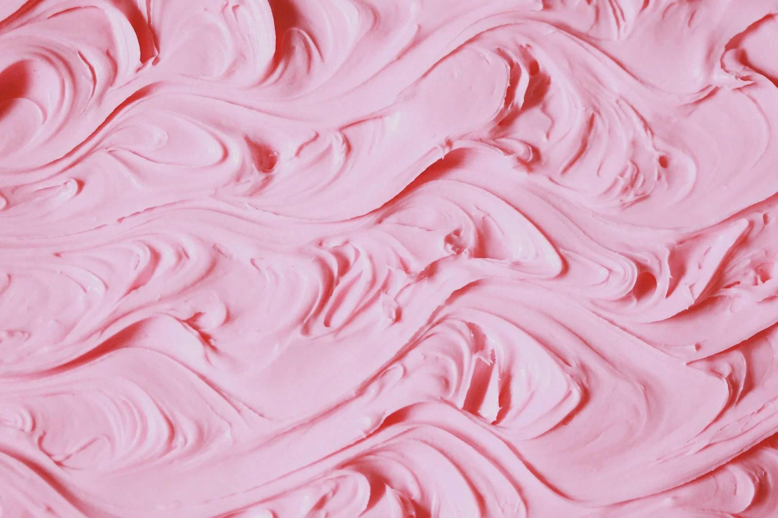 Close-up view of pink swirled frosting or cream with smooth, textured patterns.
