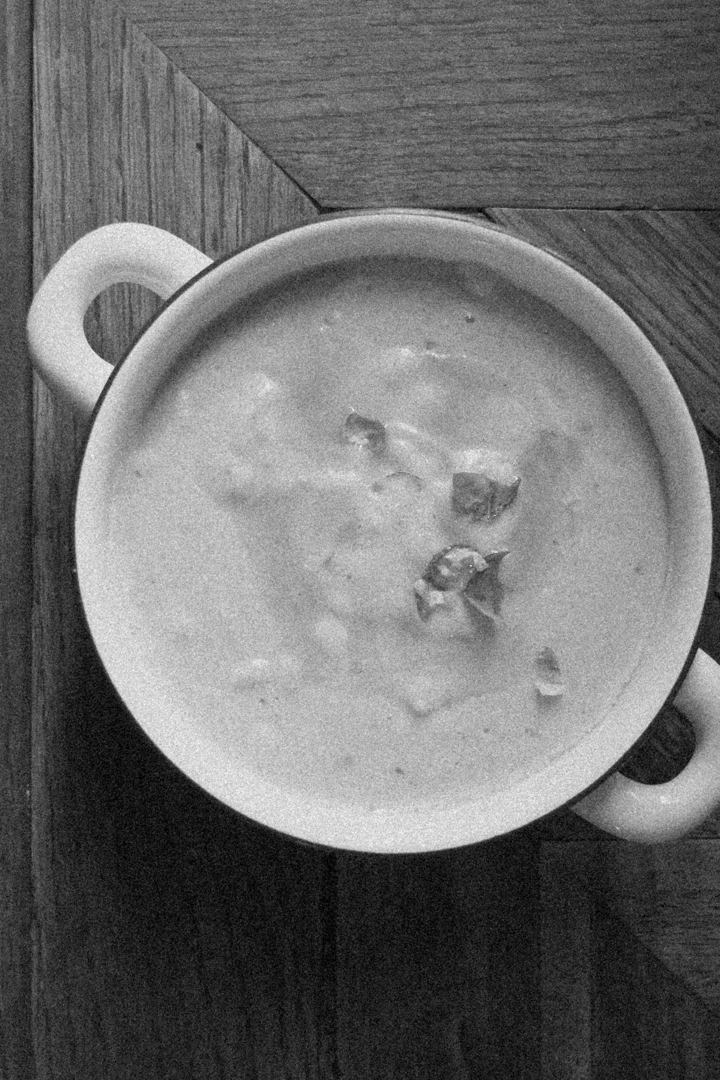 Une tasse blanche contenant une soupe avec quelques morceaux visibles, placée sur une surface en bois.