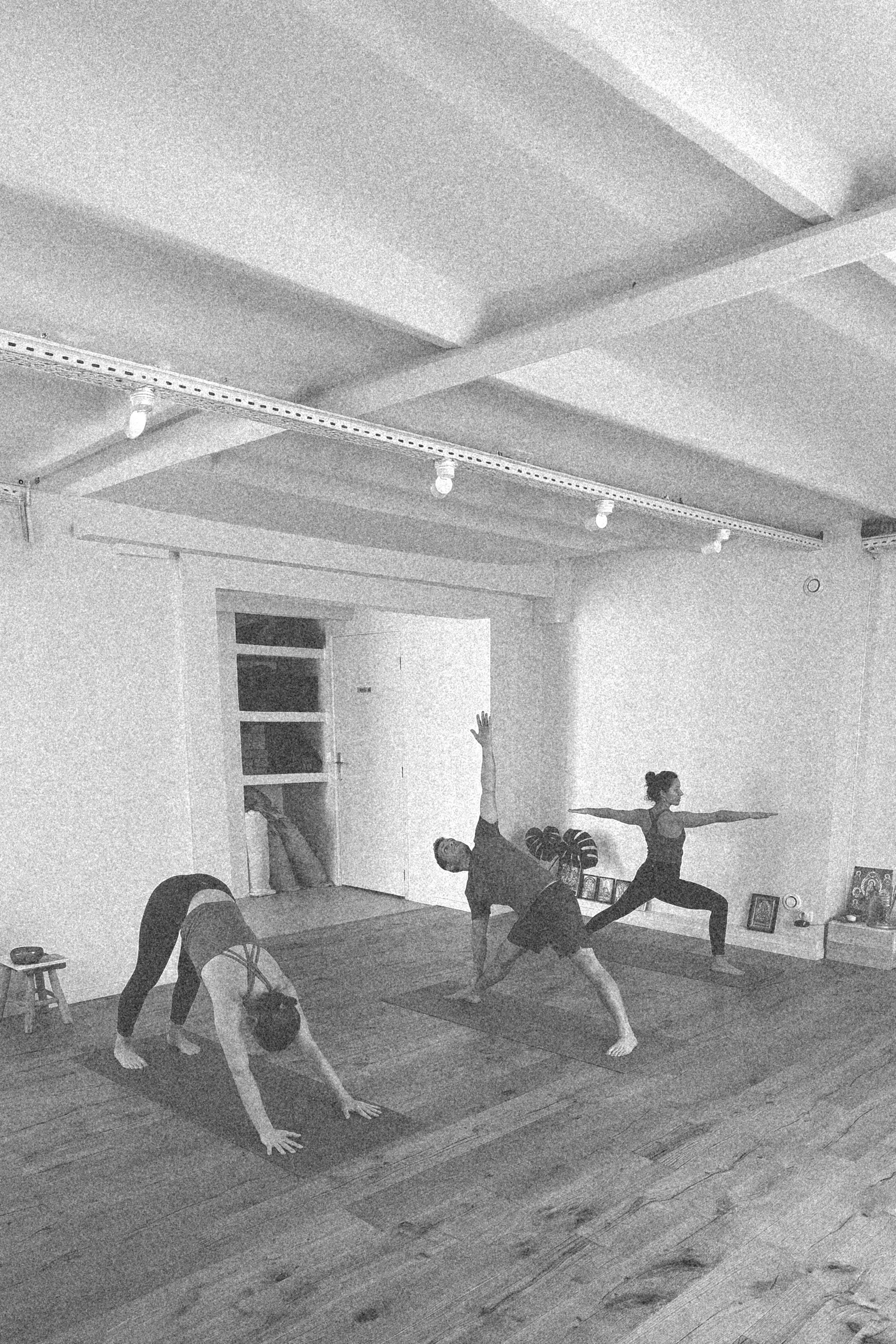 Cinq personnes pratiquent le yoga ou la méditation dans une salle intérieure, avec des tapis de yoga et des cadres au sol.