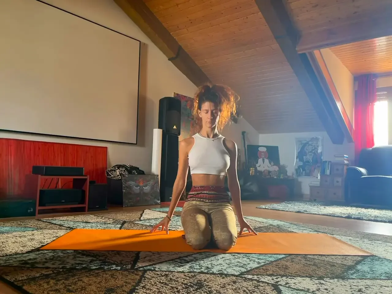 Mujer practicando yoga en una alfombra en una habitación con paredes de madera y arte en las paredes, con luz natural entrando por una ventana
