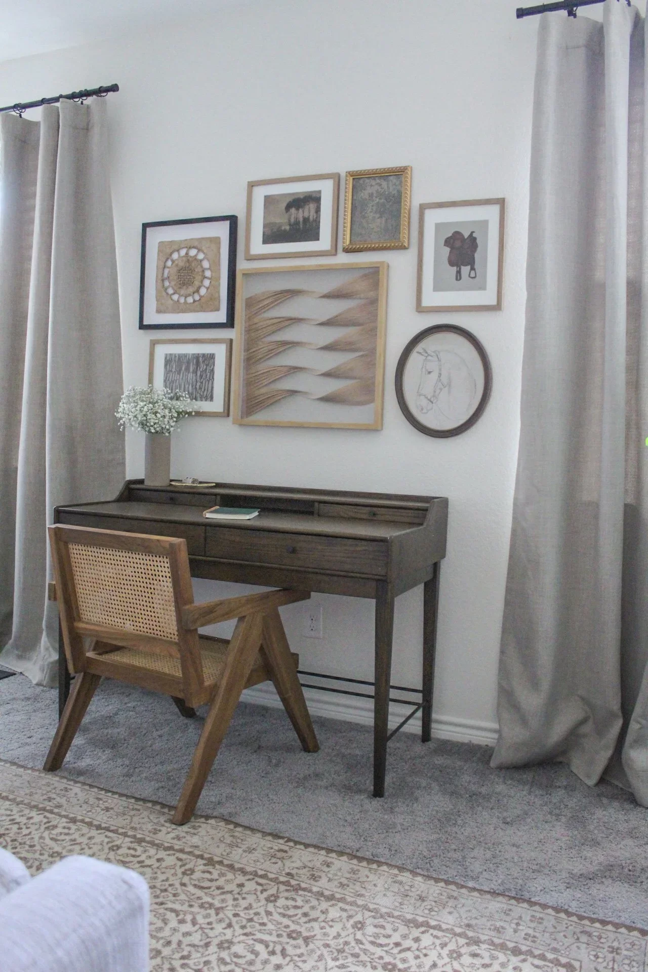 Living room corner with a desk, wooden chair, framed wall art, and beige curtains.