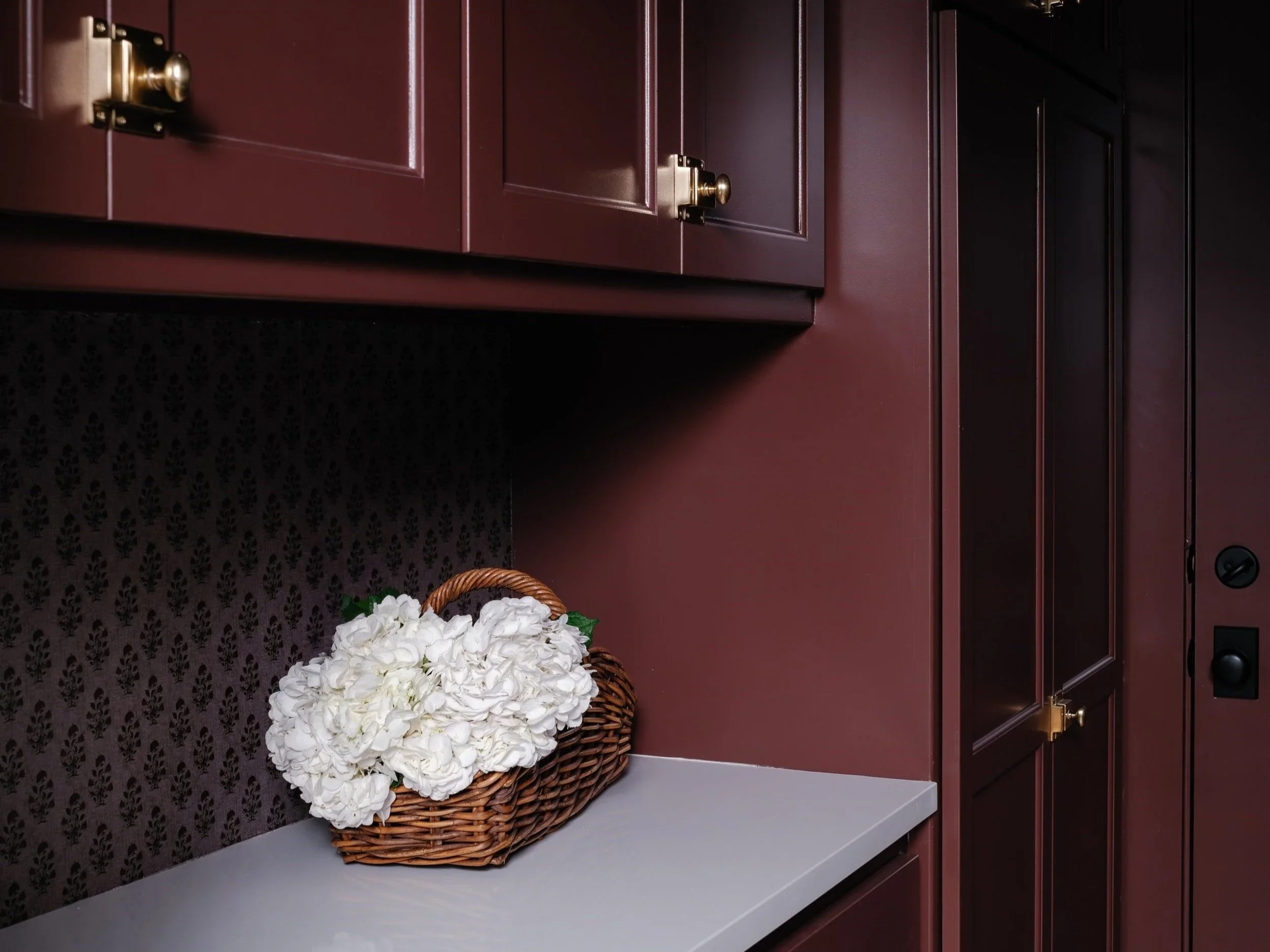 A basket filled with white flowers placed on a white countertop next to dark wooden cabinets.