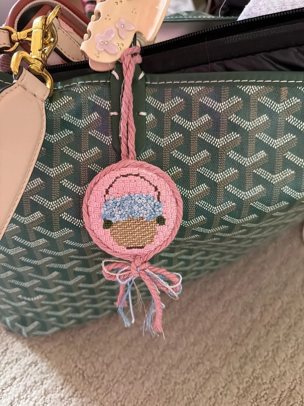 A pink crocheted keychain with a cupcake design, hanging from a bag with a patterned green and brown surface.