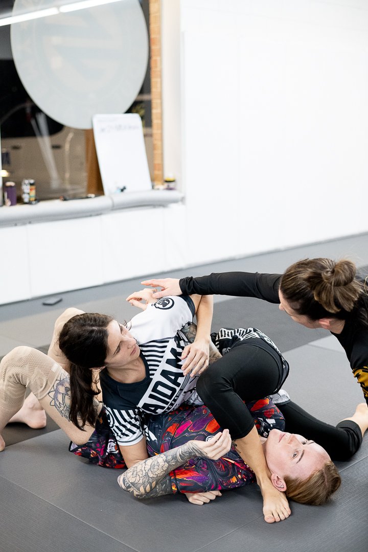 Two women practicing Brazilian Jiu-Jitsu on a mat, with one woman applying a chokehold on the other.