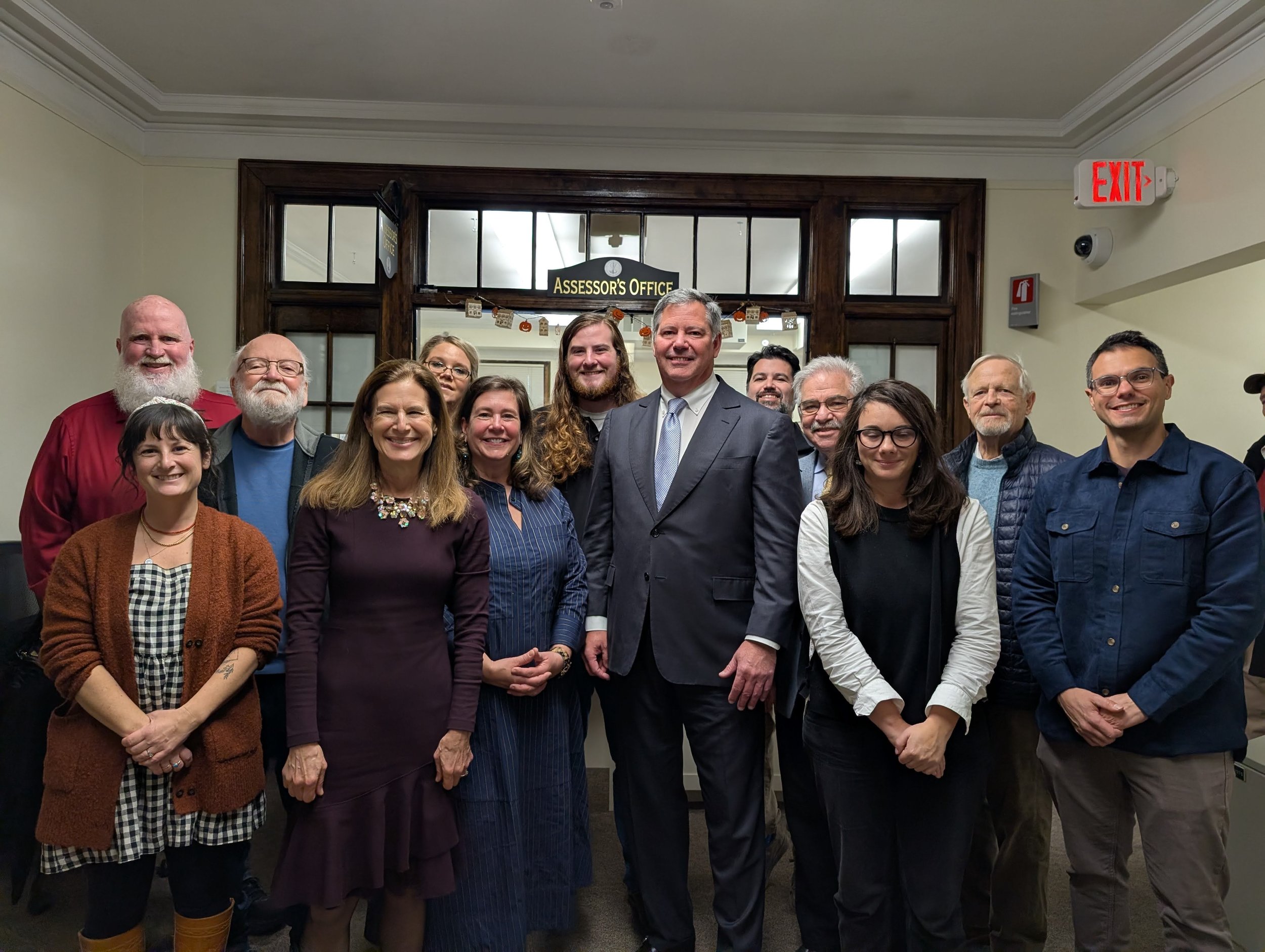 Group of elected Stonington leaders standing together inside Town Hall with Connecticut Lt. Governor, with some smiling and facing the camera.