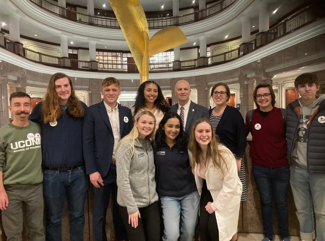 Group of young adults and a man in a lobby with a chandelier overhead, posing for a photo.