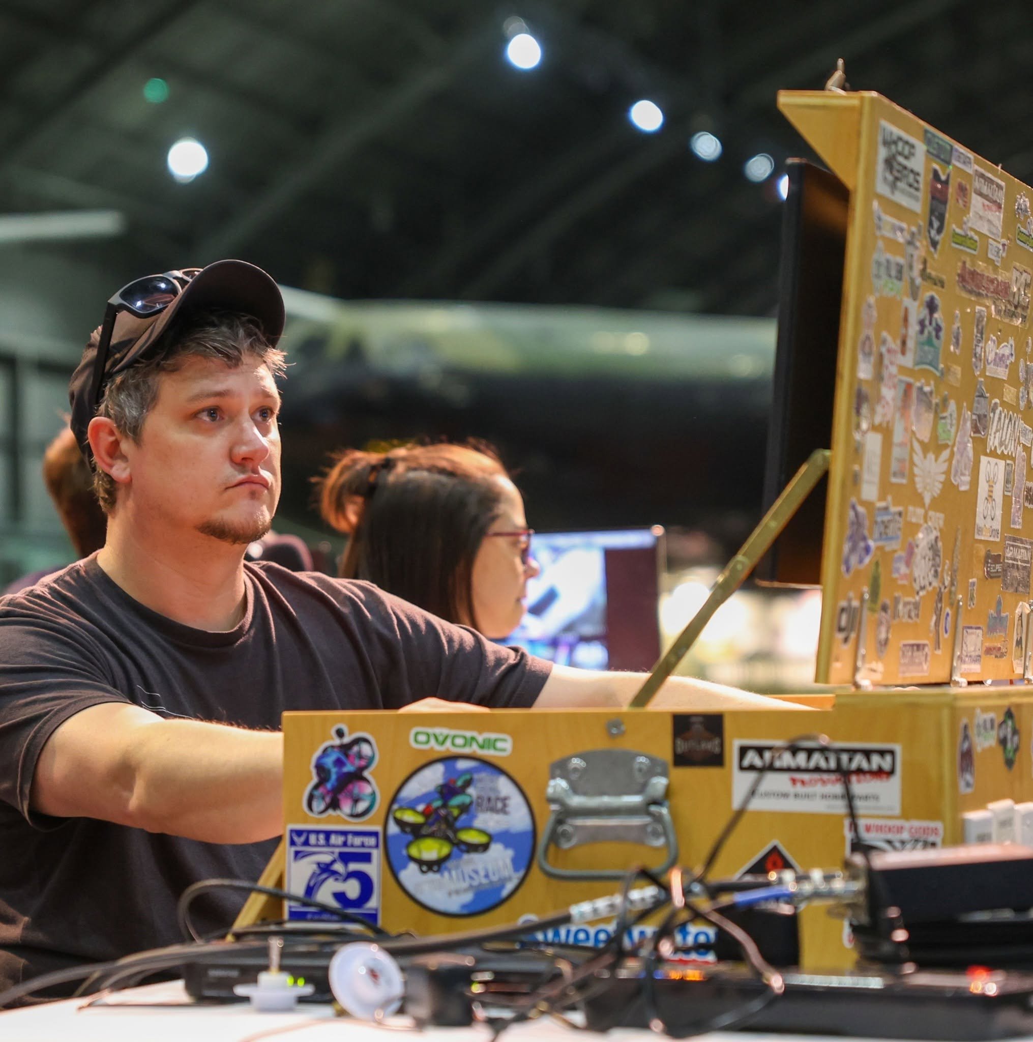 A young man seated at a computer, directing an indoor drone race event.