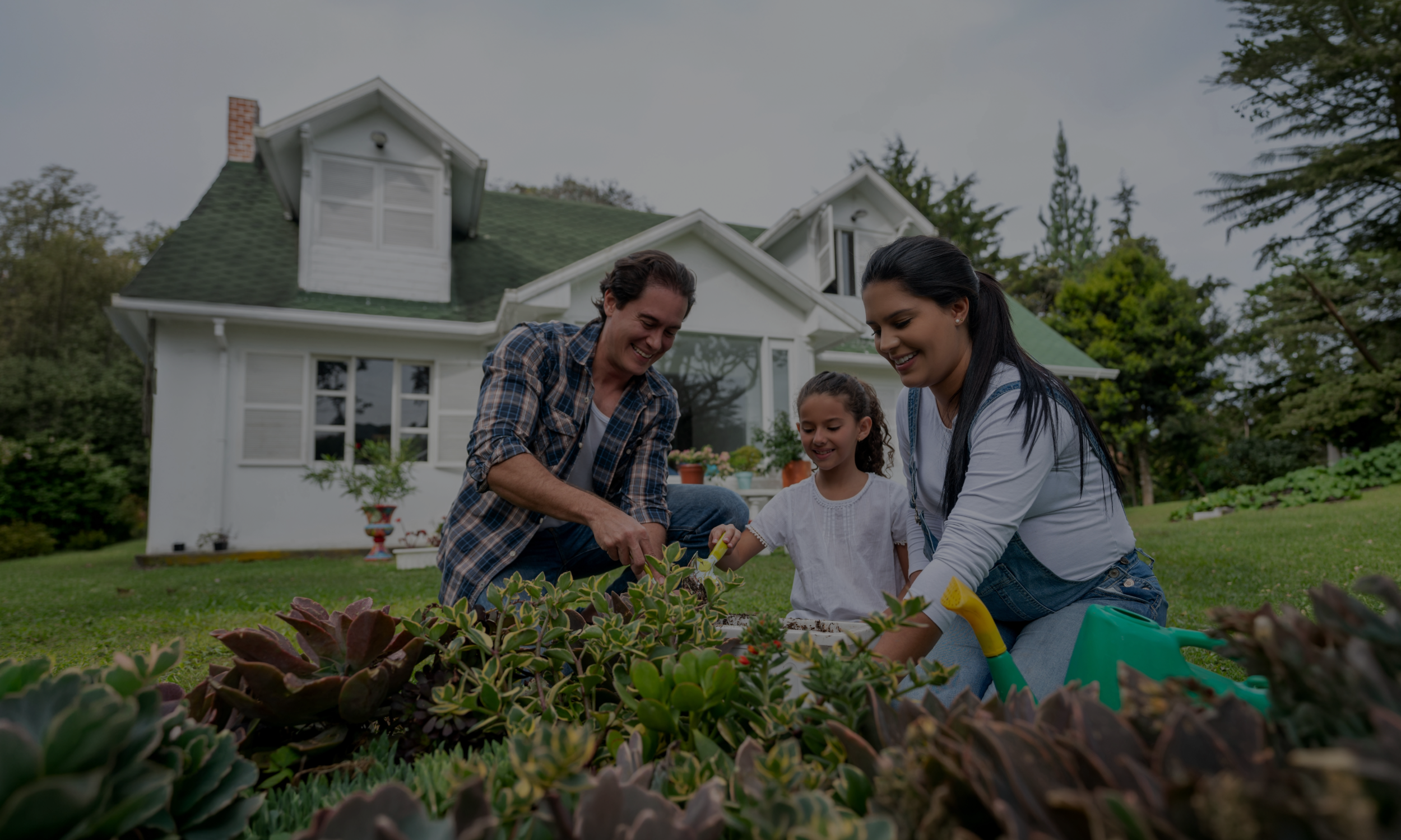 Family sitting on porch stairs of a white two-story house with black shutters and a large front yard during daytime.