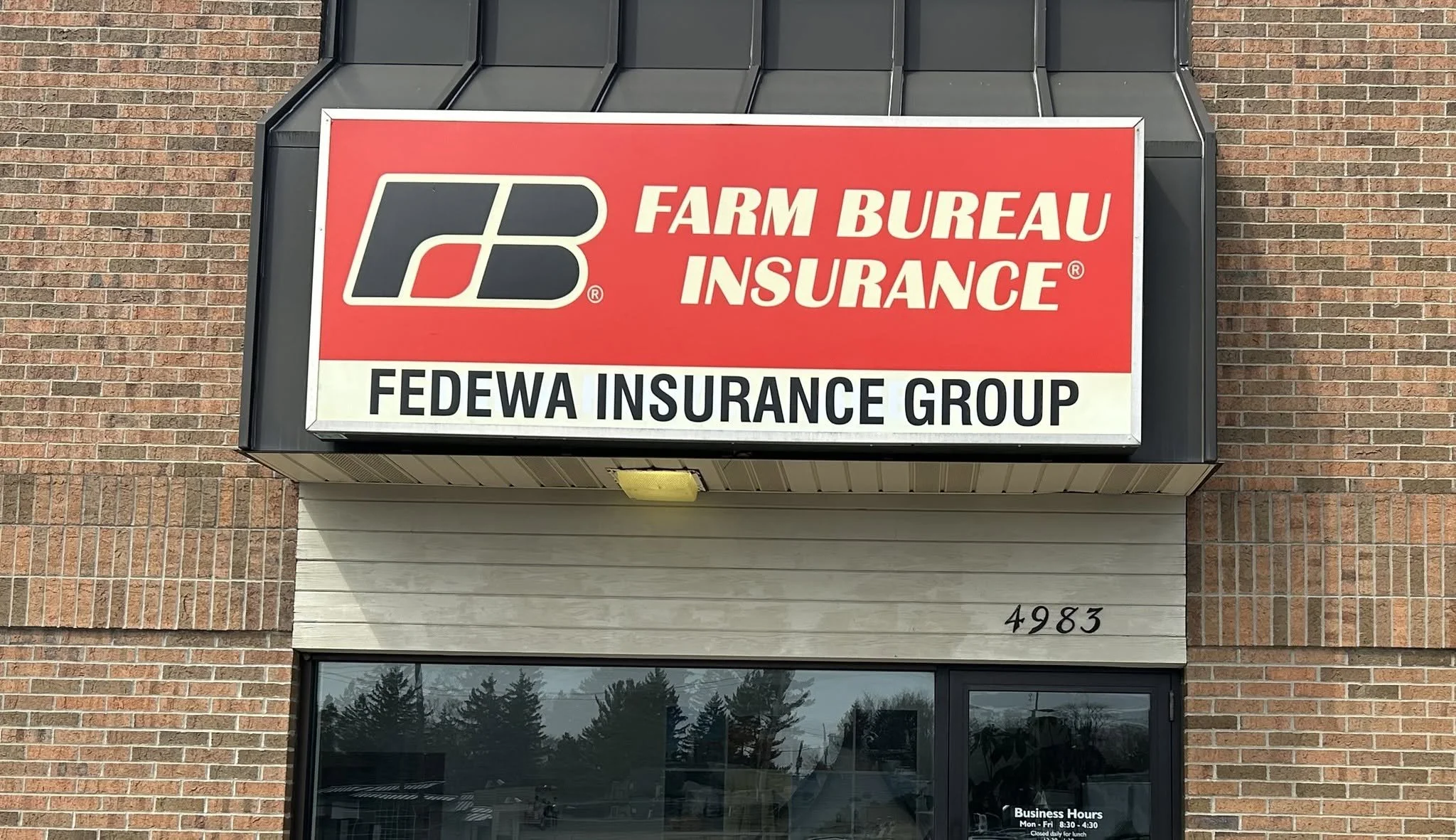 Sign for Farm Bureau Insurance at a brick building, with business hours listed below.