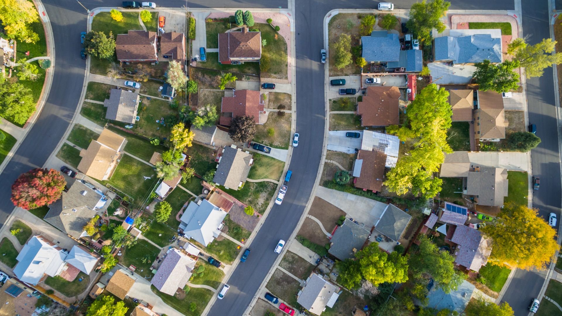 Aerial view of a residential neighborhood with houses, trees, and parked cars along the streets.